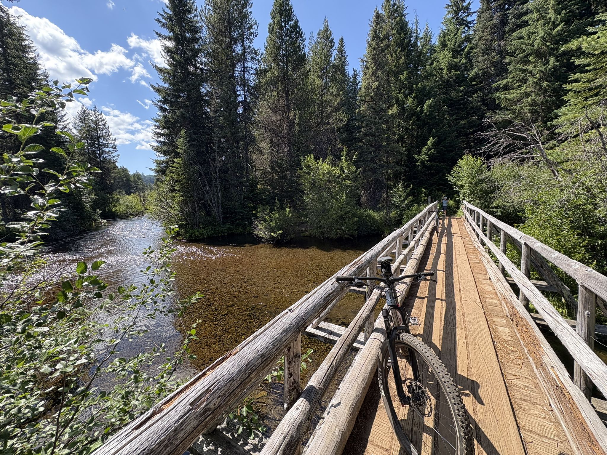 A bicycle rests on a long wooden bridge over a shallow, clear river. - Timothy Lake – Timothy Lake loop from Gone Creek Campground