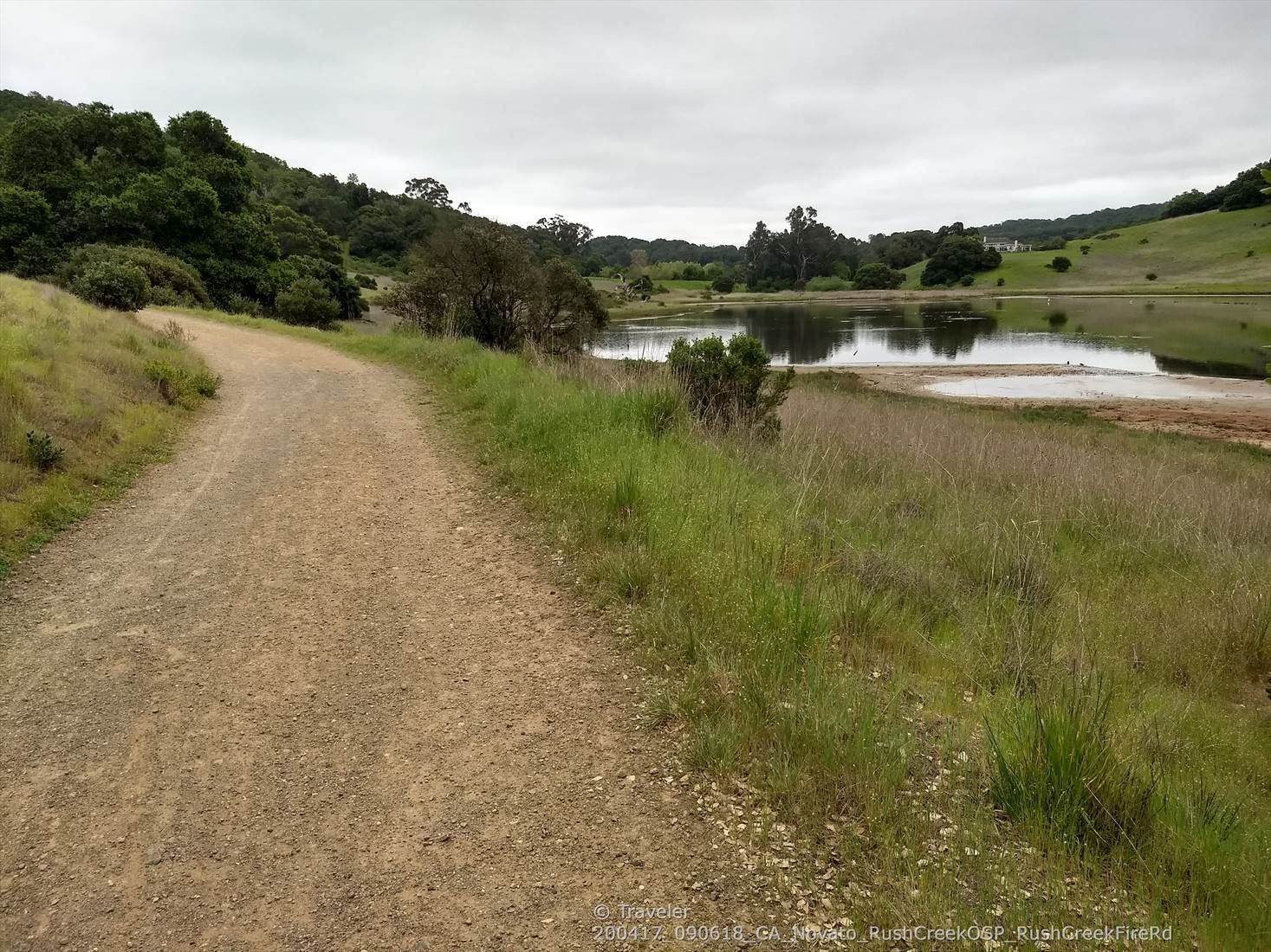 A dirt path alongside a calm lake with grassy hills under an overcast sky. - Rush Creek and Bahia Trail Loop