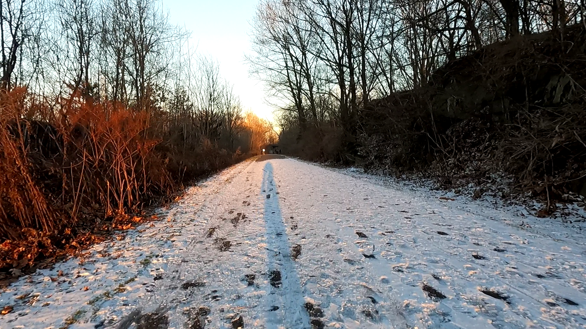 Snowy path with footprints and long shadow, sun setting through bare trees. - Poughkeepsie to Mills Memorial State Park loop
