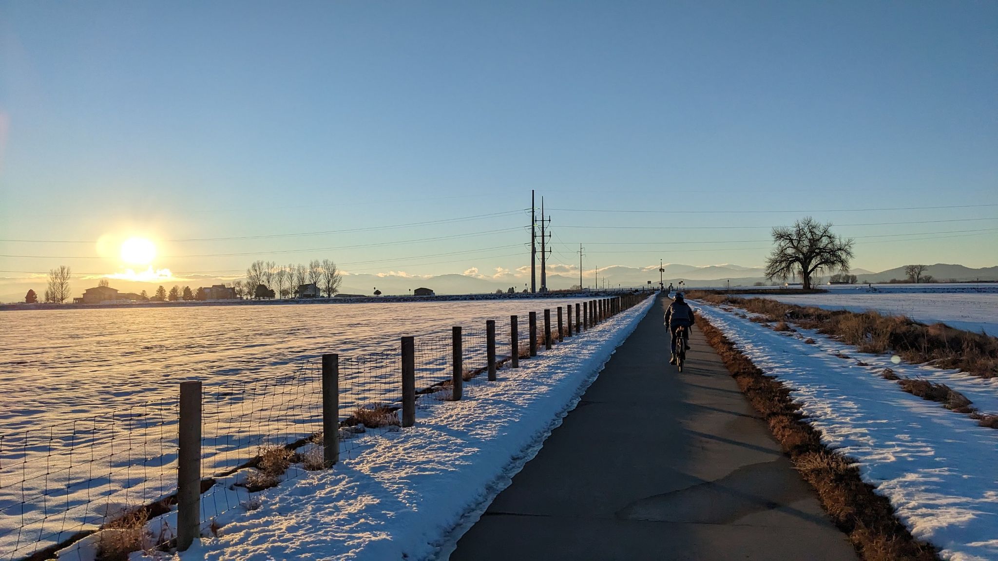 Cyclist on a snowy path at sunrise, with fields and distant mountains. - Loveland Recreation Trail Loop