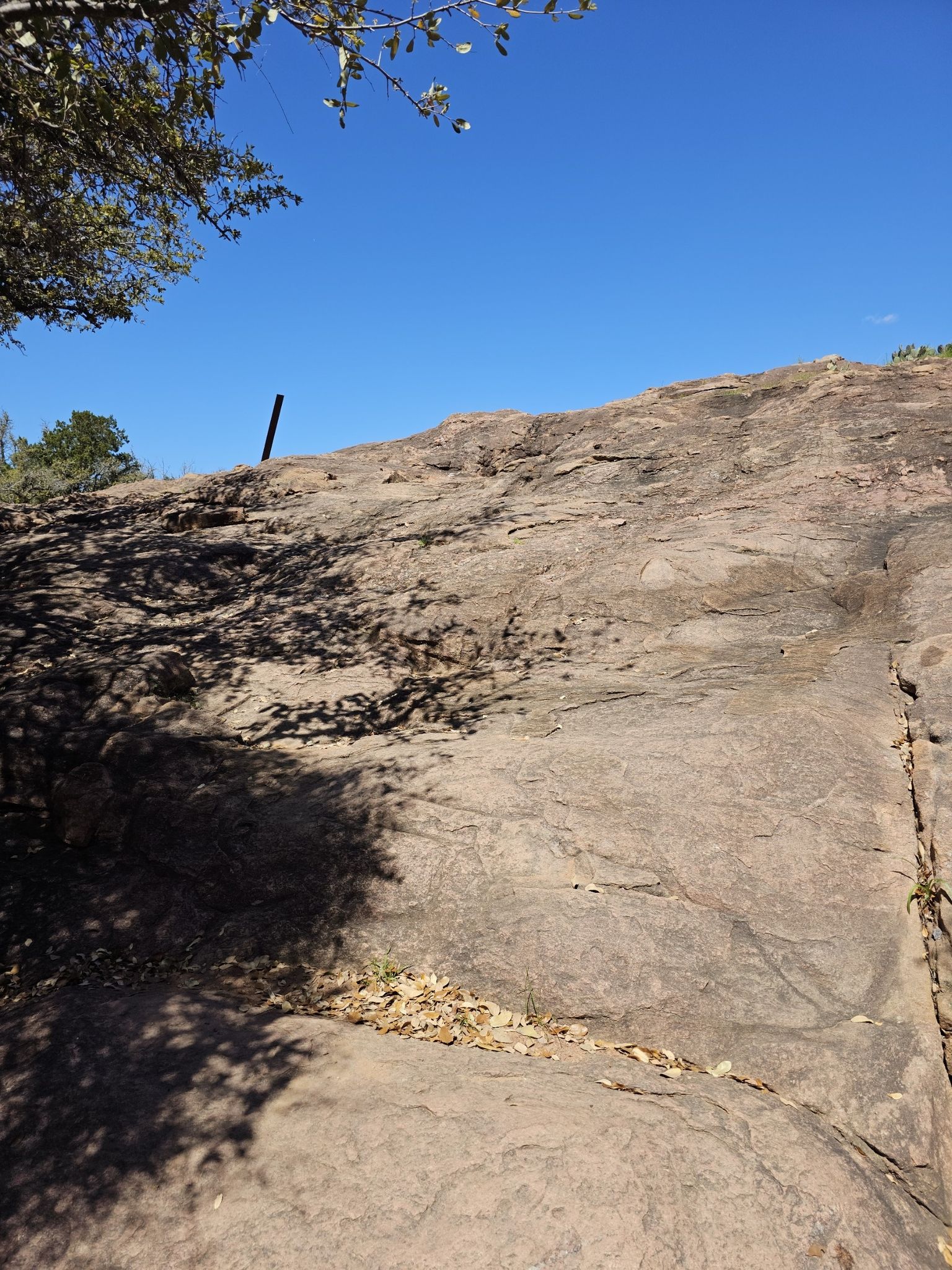 A large, smooth rock face with shadows and a clear blue sky above. - 1000ft overlook of Inks Lake loop from Inks Lake State Park