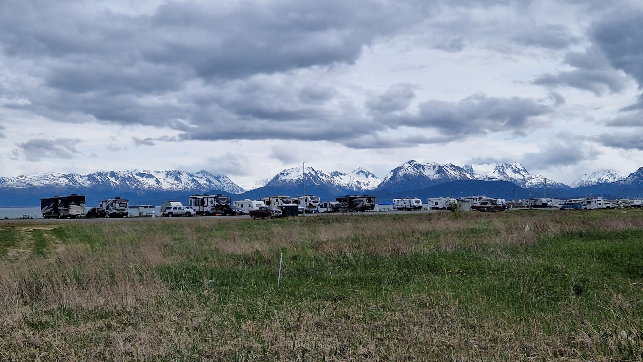 Line of RVs parked along a road with majestic snow-capped mountains behind. - Nick Dudiak Fishing Lagoon – Louie's Lagoon loop from Homer Spit