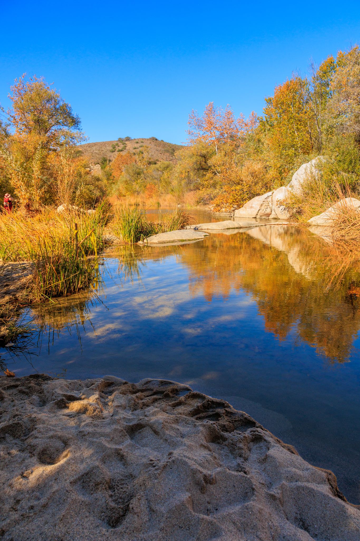 Calm water reflects blue sky and colorful autumn trees in a rocky landscape. - Santa Magarita River Loop
