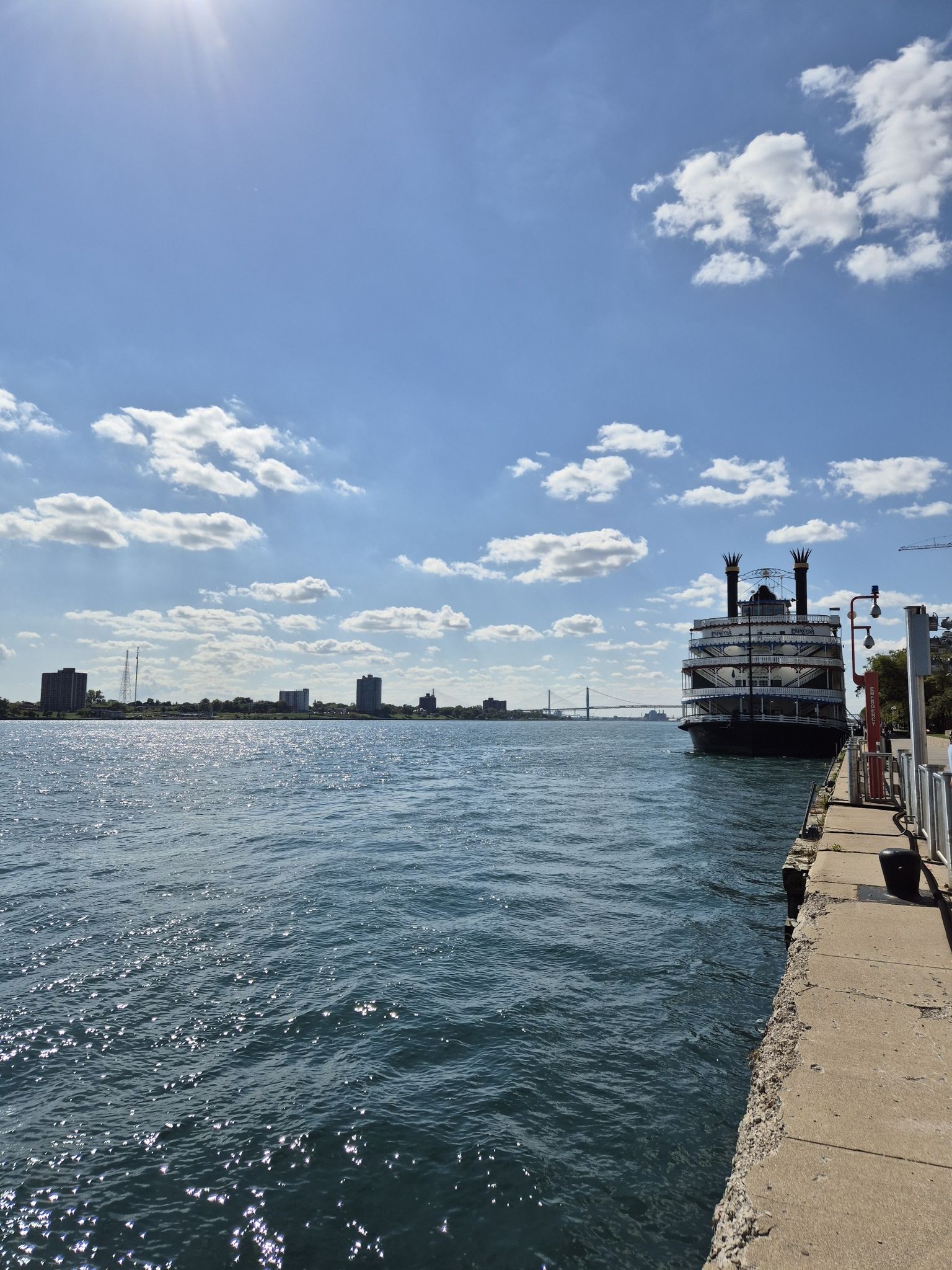 Large paddlewheel boat docked by a river, city skyline in distance, sunny day. - Renaissance Center – Gateway to Freedom Monument loop from Detroit