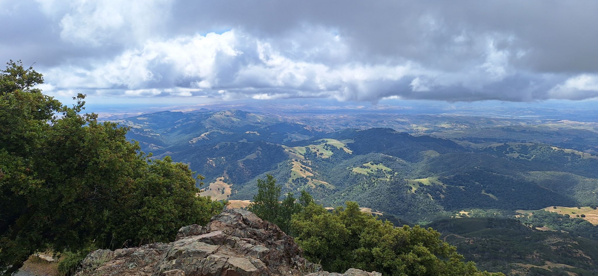 Rocky outcrop and trees overlooking a vast, cloudy mountain landscape. - Mount Diablo via North Gate and Summit Roads