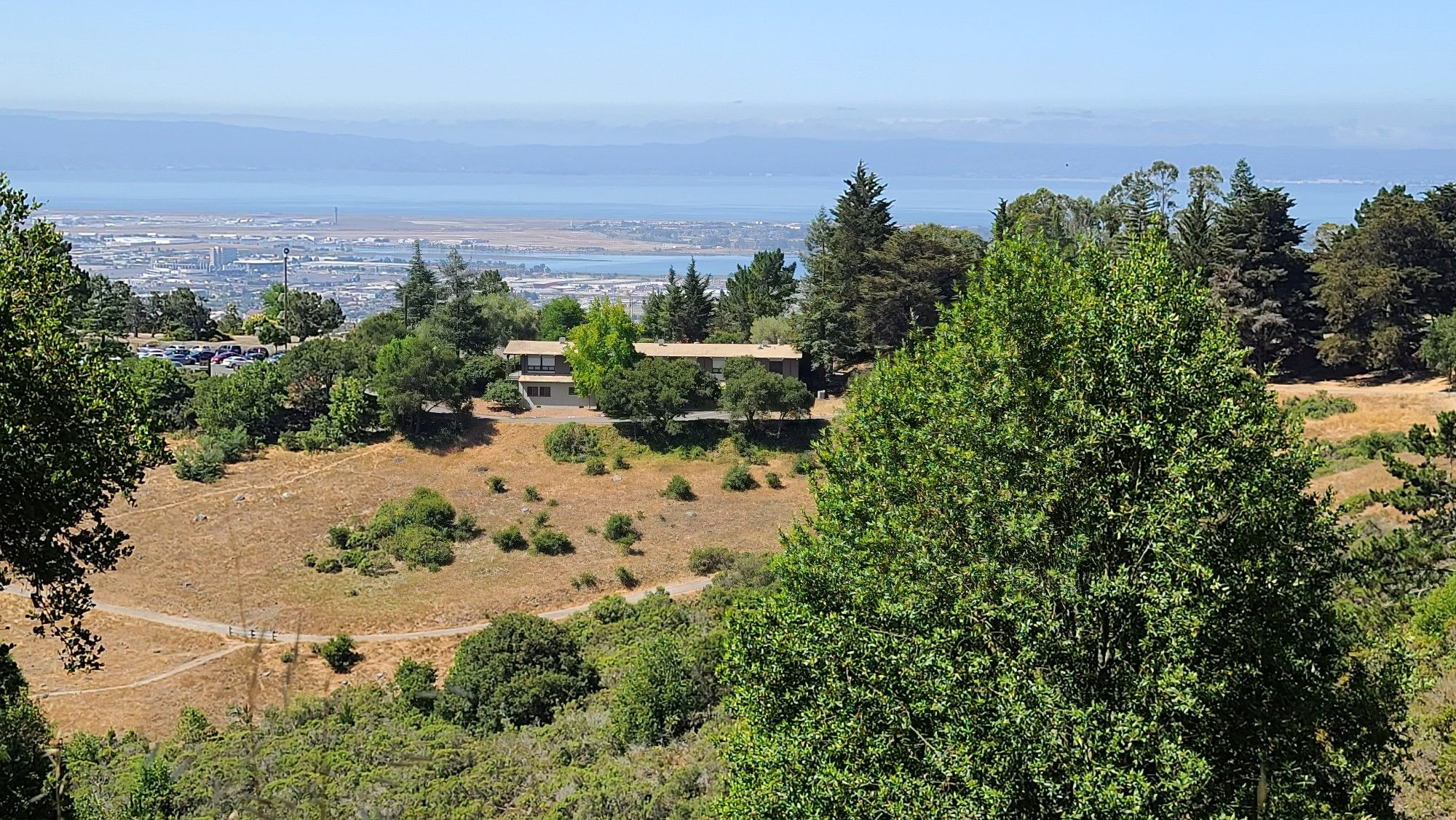 Panoramic view of dry grassy hills, scattered trees, and distant water under bright sky. - Dunn Trail
