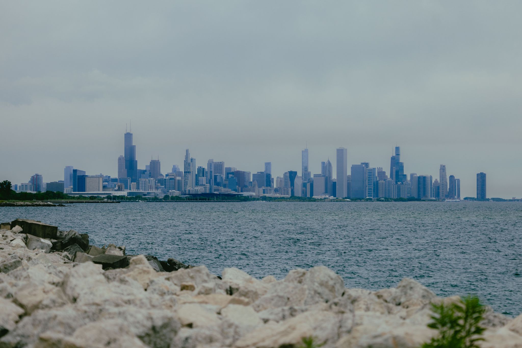 Rocky shore in foreground with a hazy city skyline across the water. - McCormick Bird Sanctuary – Burnham Wildlife Corridor loop from Cermak-Chinatown