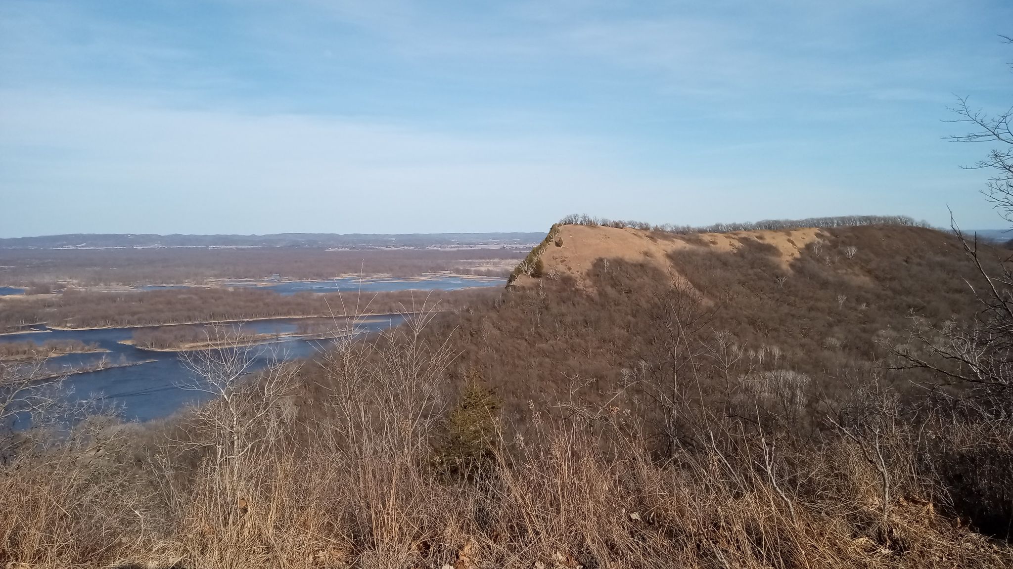 Expansive view of a river valley with a large bluff and distant water under a bright sky. - King's Bluff Trail