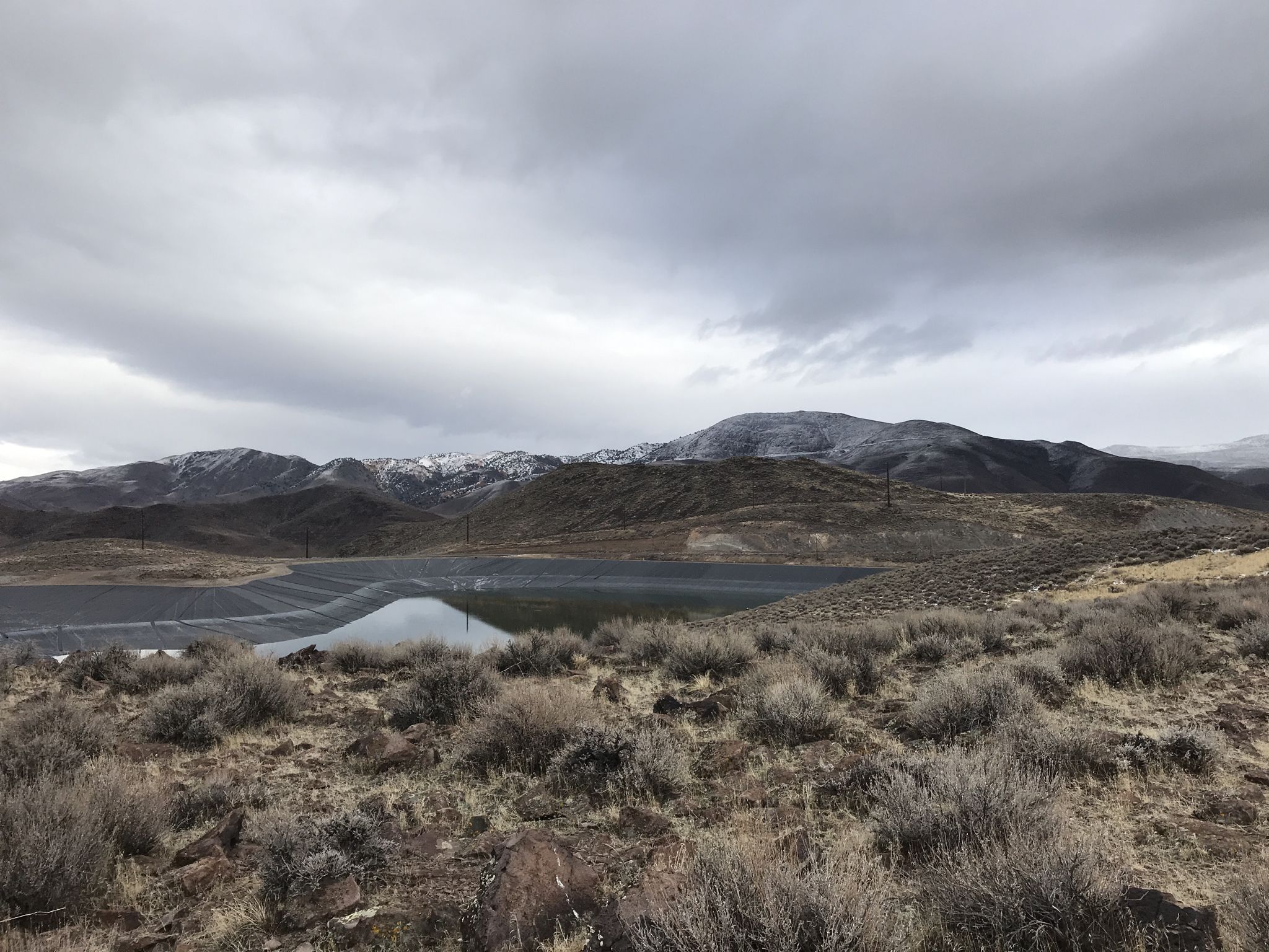 Large reservoir in an arid landscape with distant snow-dusted mountains under cloudy skies. - Huffaker Hills Peak