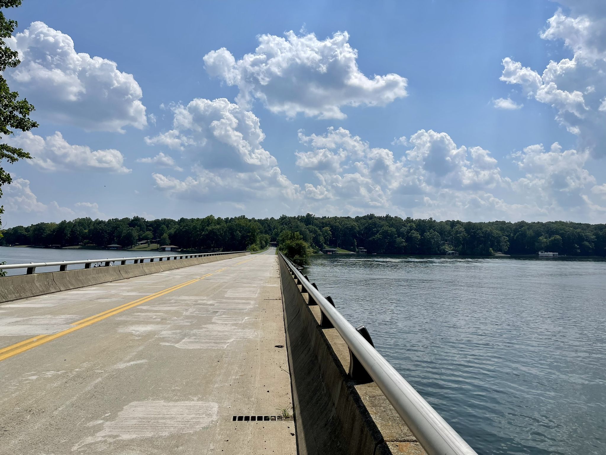 A long concrete bridge spans calm water under a bright, cloudy sky. - Lake Louisa loop from Holy Church of the Living God