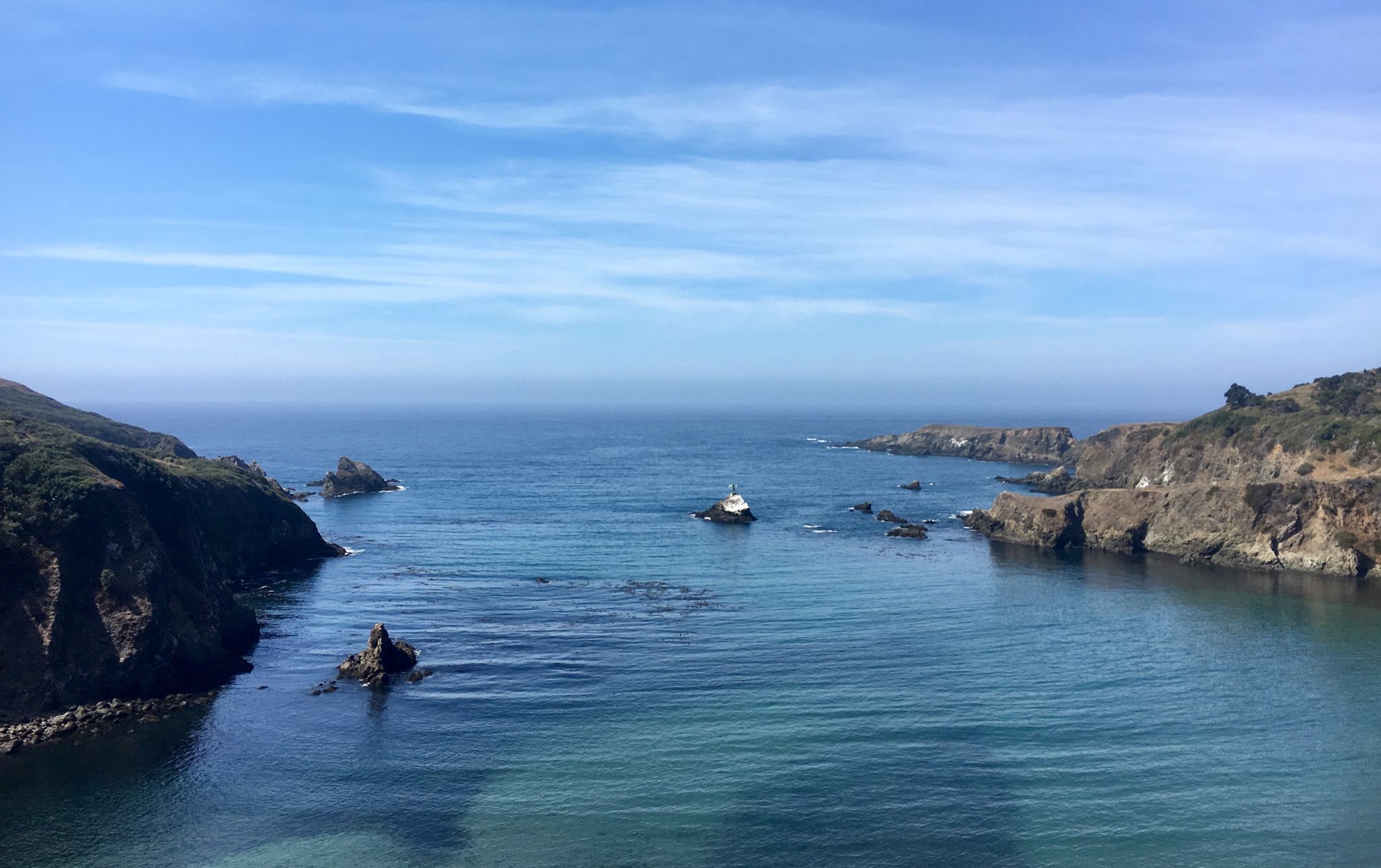 Boat in a calm ocean cove with rocky cliffs under a clear blue sky. - Mendocino - Comptche loop