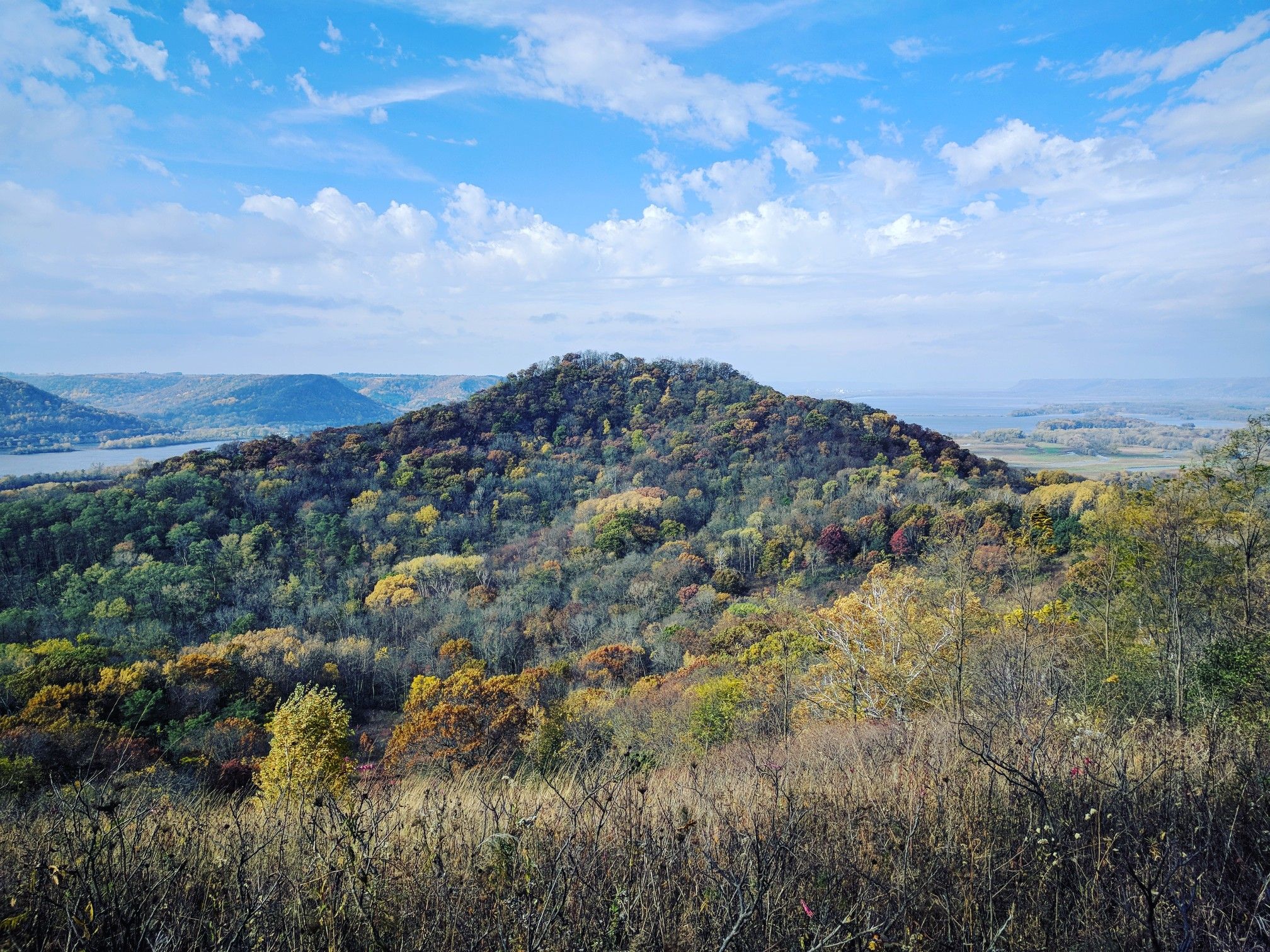 Forested hill with autumn colors overlooking a distant river under a partly cloudy sky. - White Pine Run to Reed's Run Loop