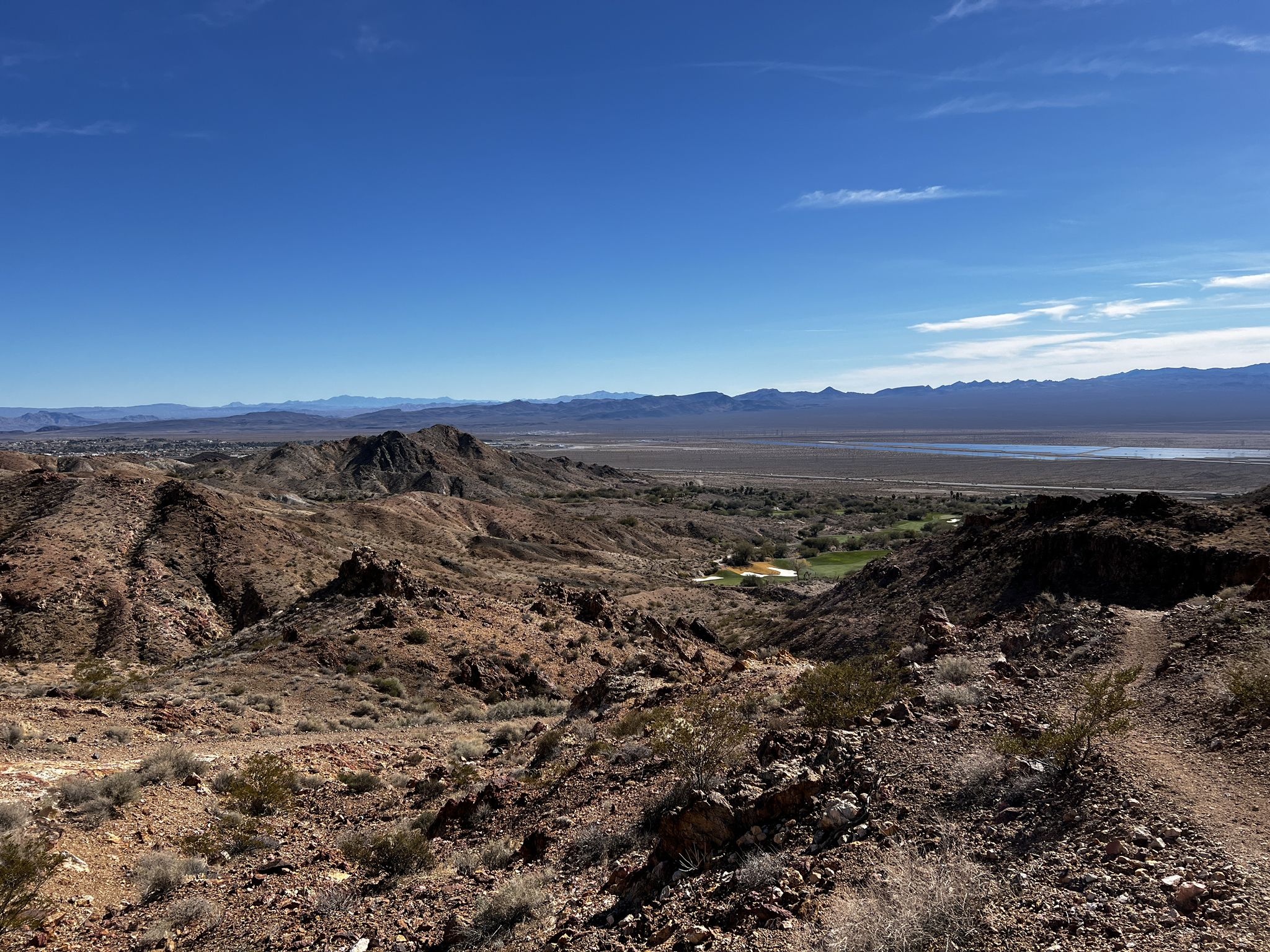 Expansive desert landscape with rocky hills, a valley, and distant water under a clear sky. - Old Vegas to Railroad Pass Trail