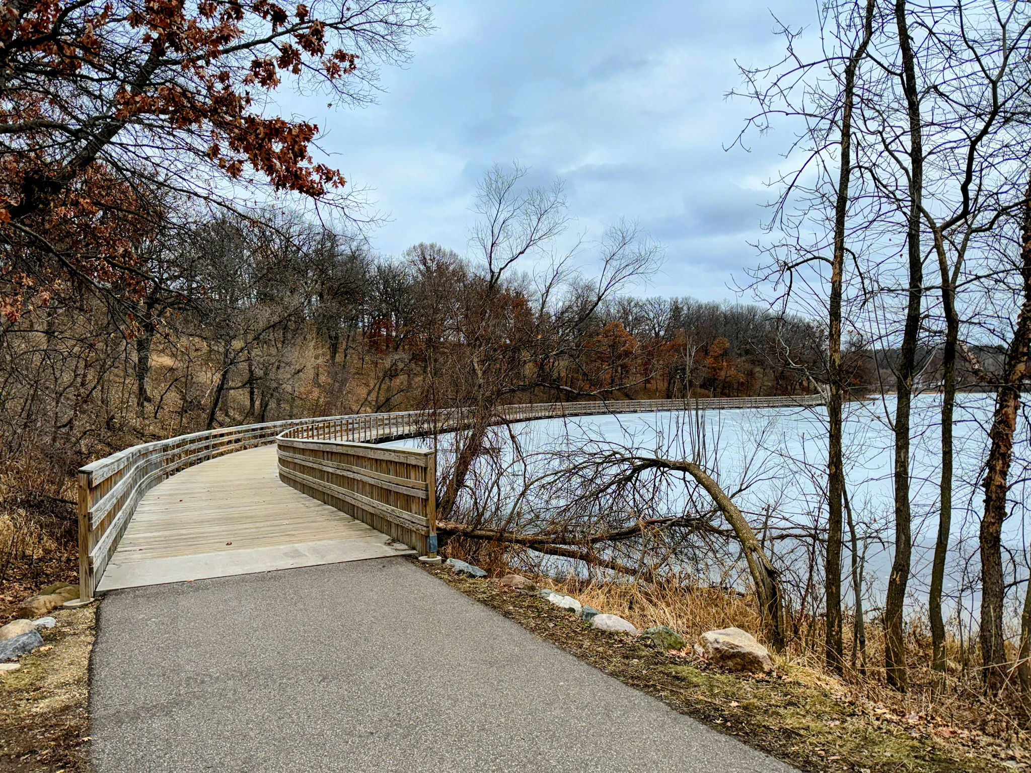 Wooden boardwalk curves along a frozen lake under an overcast sky. - Voyageur Trek Loop