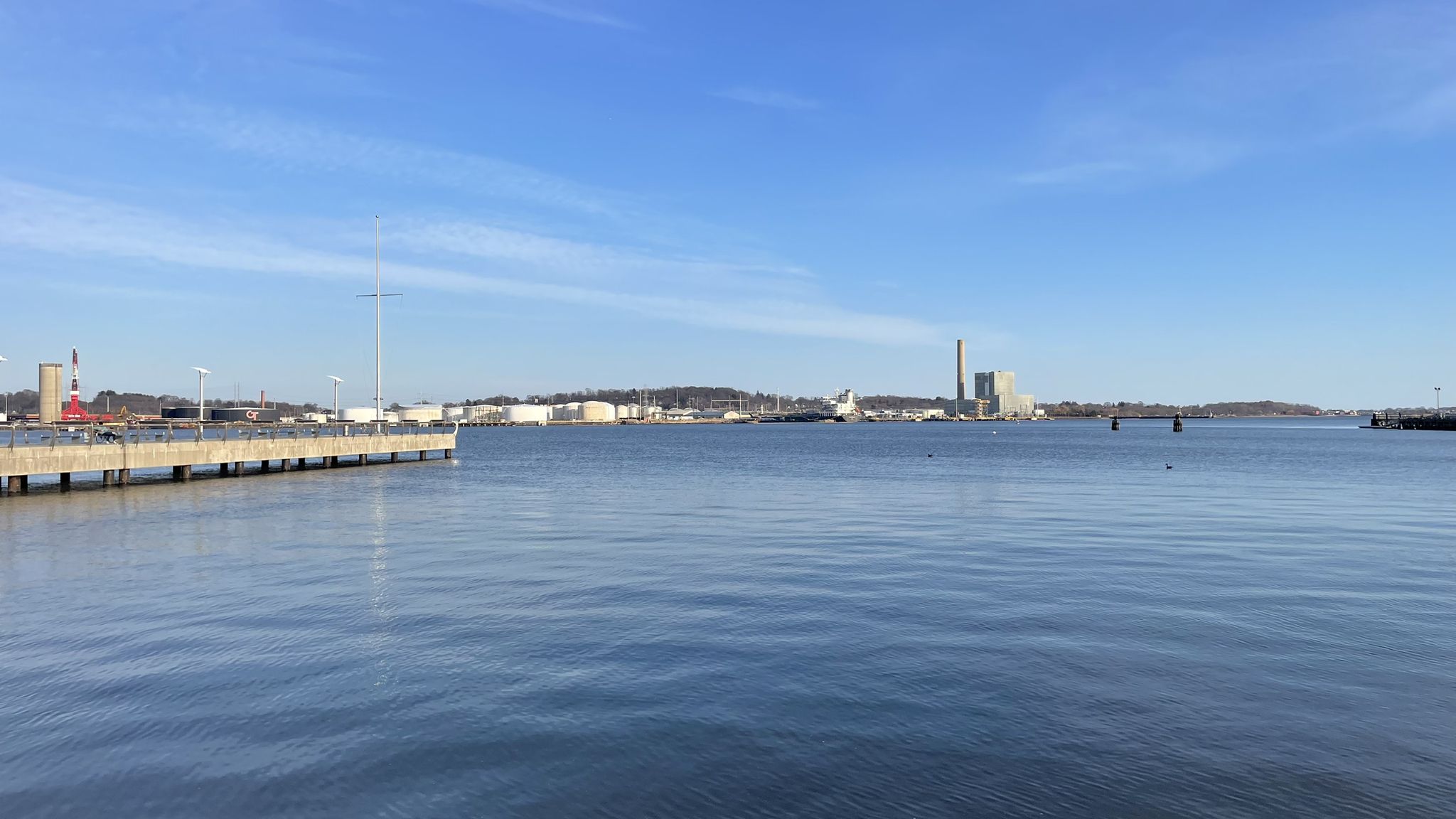 Wide water body with a pier and distant industrial buildings under a clear sky. - New Haven Downtown and Long Wharf Loop