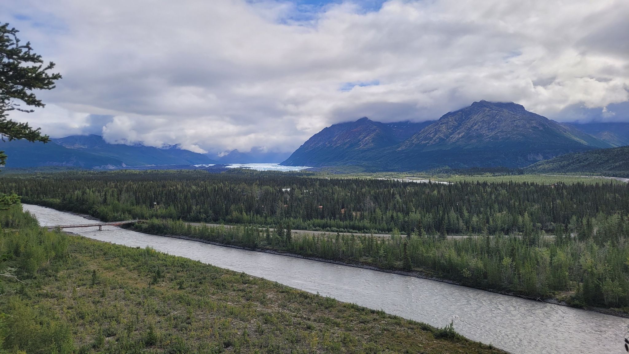 Overcast view of a wide river, forest, and distant mountains with a body of water. - Edge Nature Trail