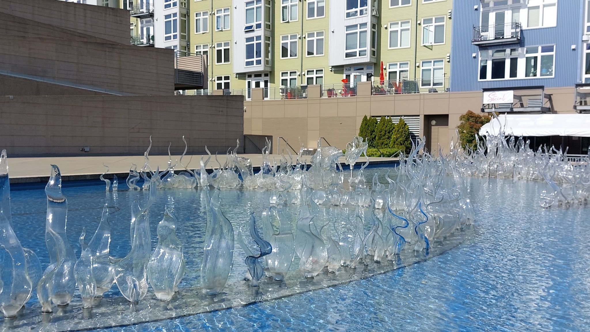 Clear glass sculptures in a sunny water fountain with buildings behind. - Thea Foss Esplanade and Prairie Line Trail