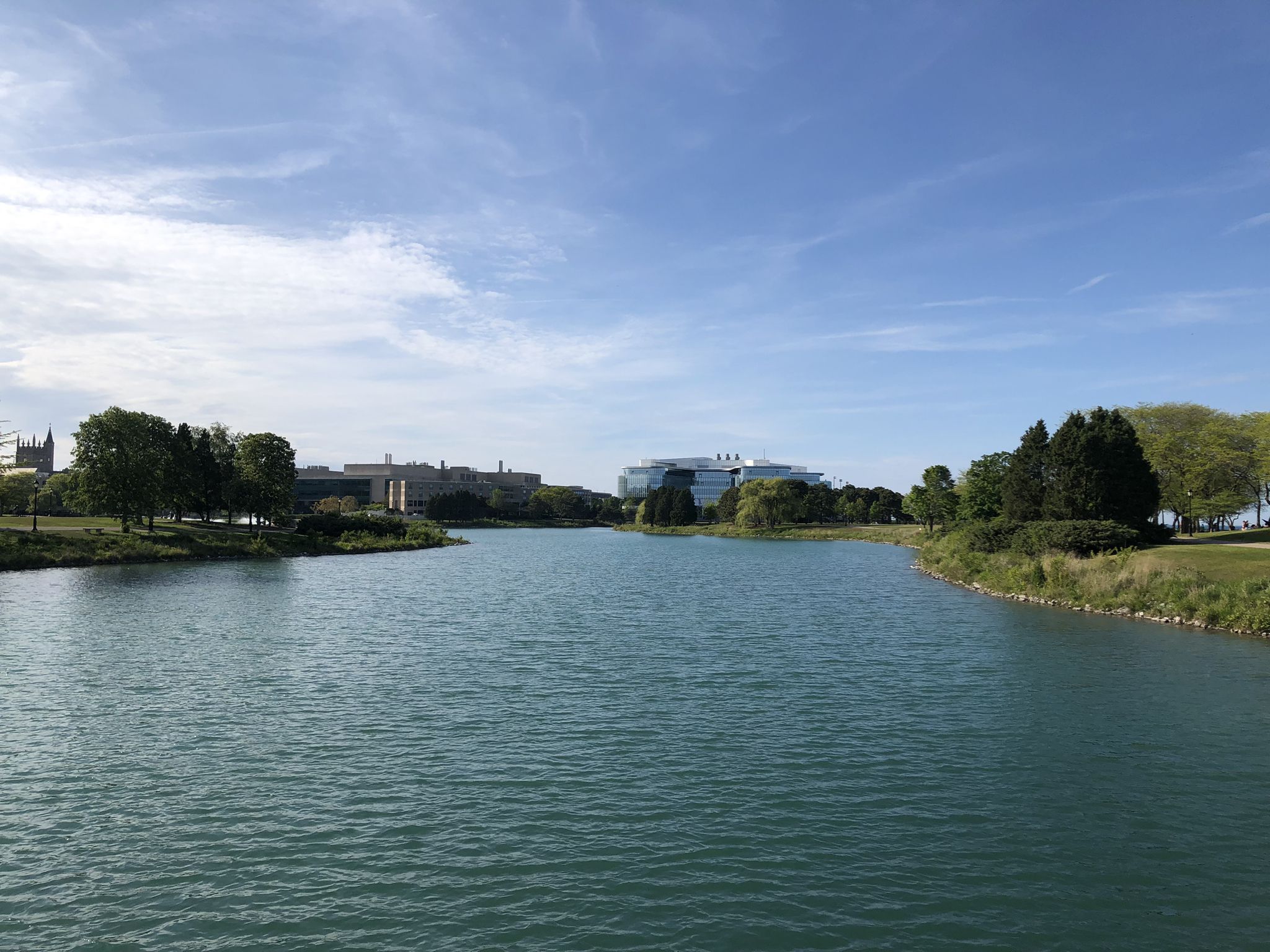 Wide river with green banks and distant buildings under a bright blue sky. - Evanston Lakefront Trail