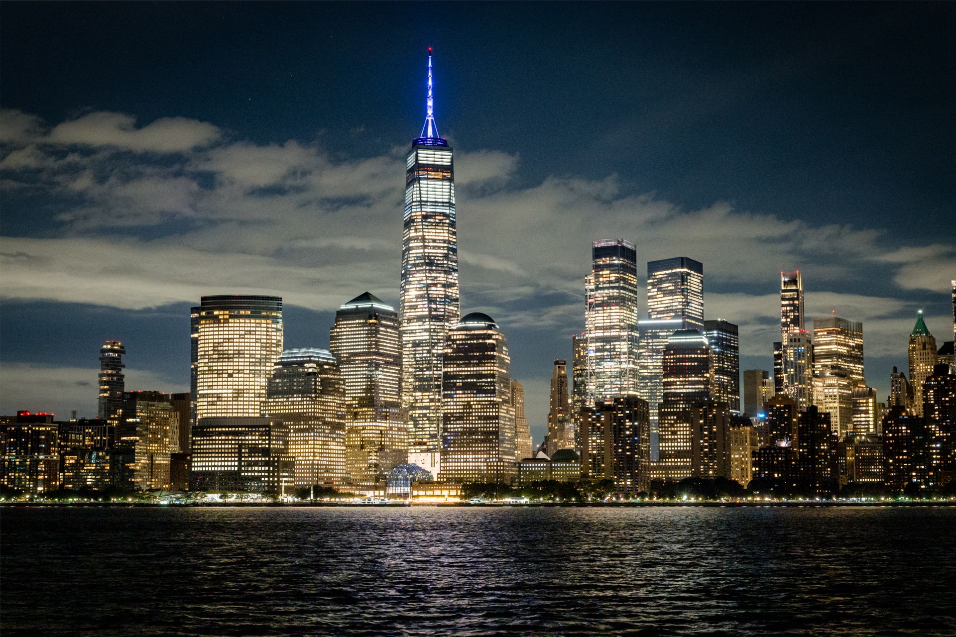 Illuminated city skyline at night, with reflections on dark water under a cloudy sky. - Morris Canal Greenway