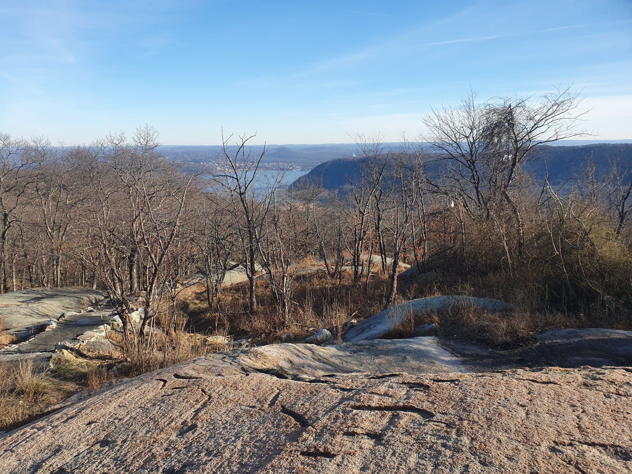 Rocky foreground overlooks a valley with a river and bare trees under a clear sky. - Bear Mountain Loop Trail