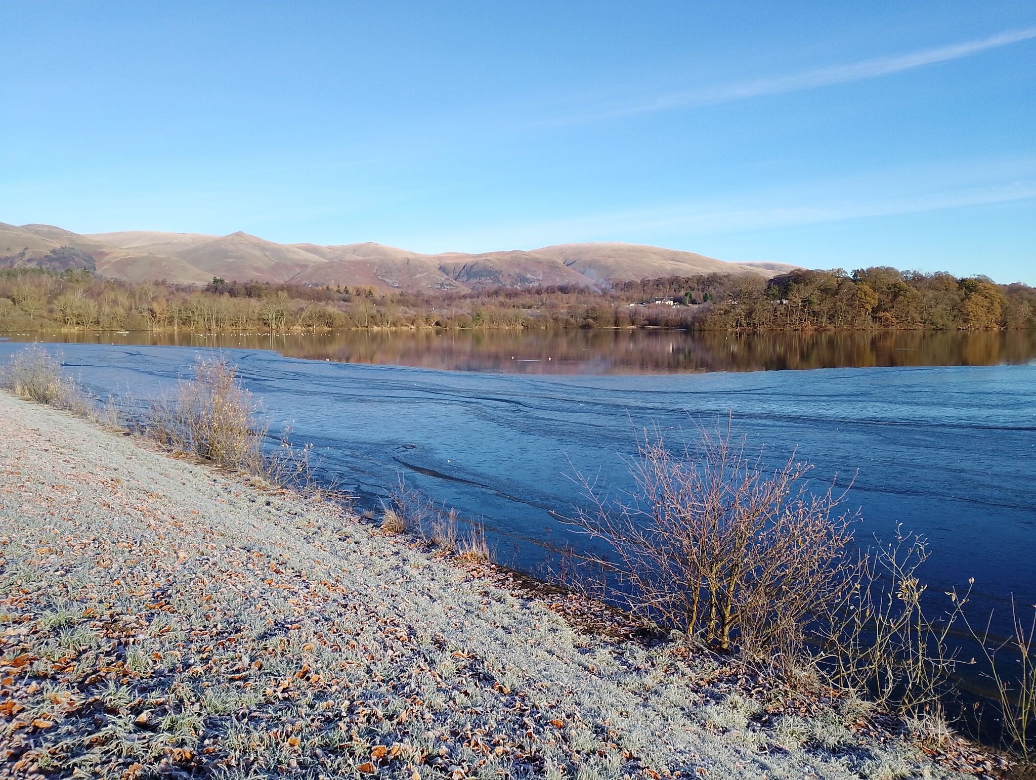 Gartmorn Dam partially frozen with the Ochil hills in the background.