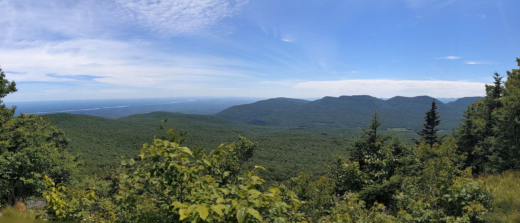 Panoramic view of lush green mountains and a distant valley under a bright blue sky. - Roundtop Mountain and Kaaterskill High Peak Loop
