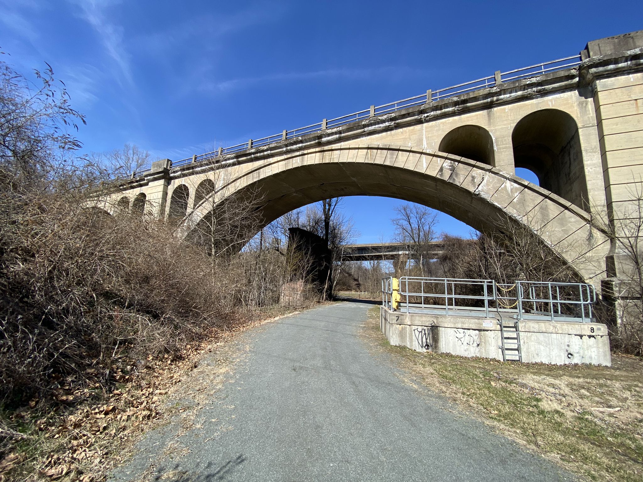 Sunny view of a massive concrete arched bridge over a gravel path. - Mohnton loop