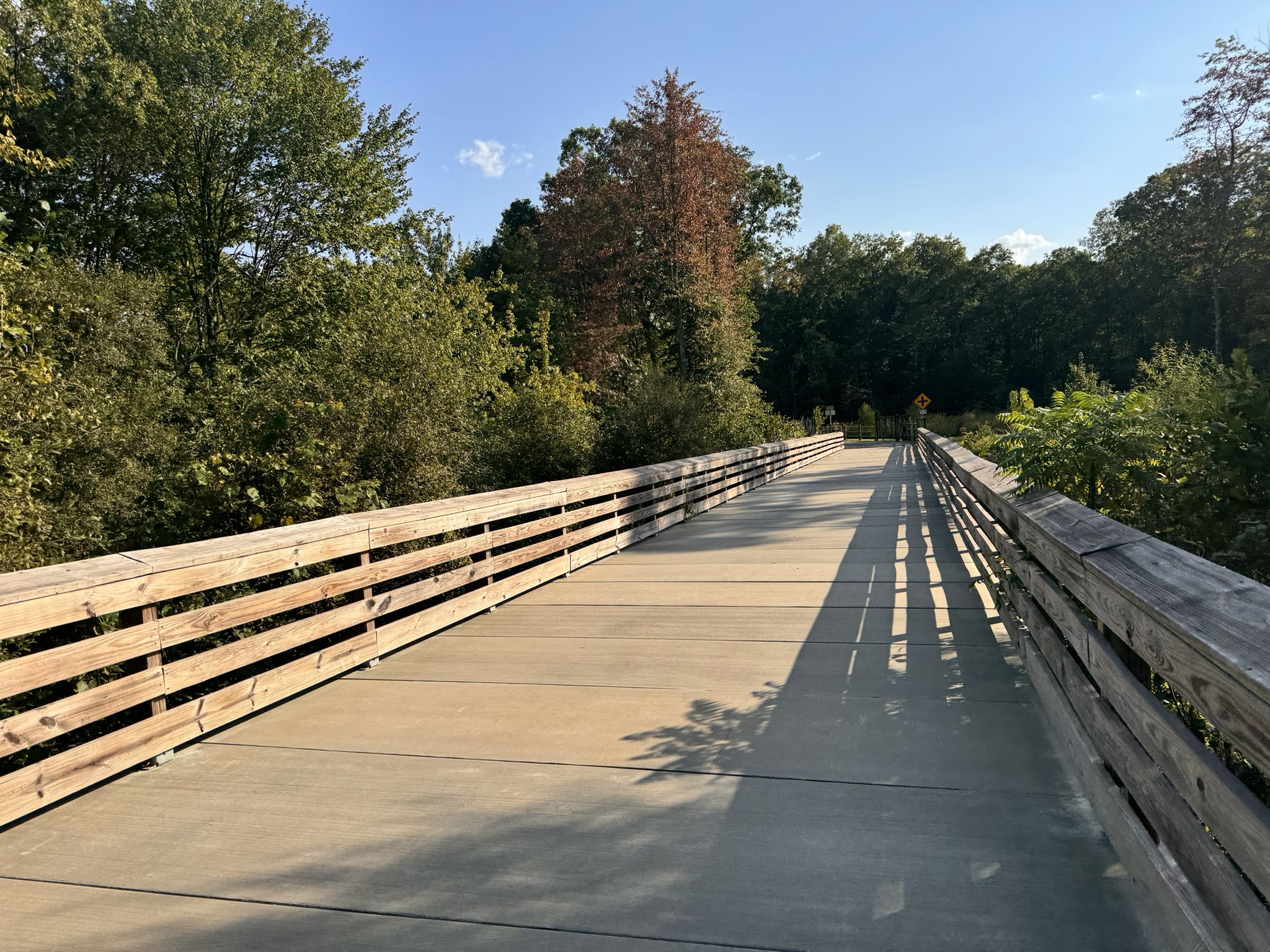 Long wooden bridge extending through a green forested area on a sunny day. - Running loop from Farmington Canal Line State Park Trail
