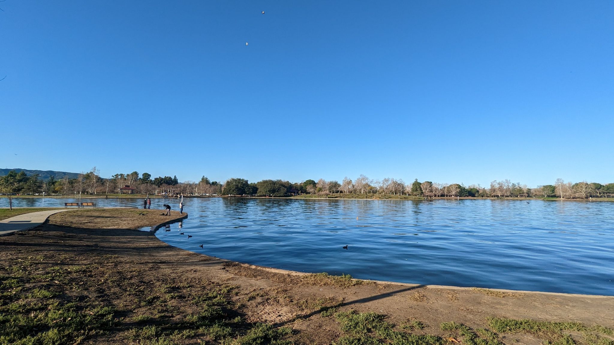 Bright daylight over a wide lake with a few people on the shoreline. - Lake Balboa Trail