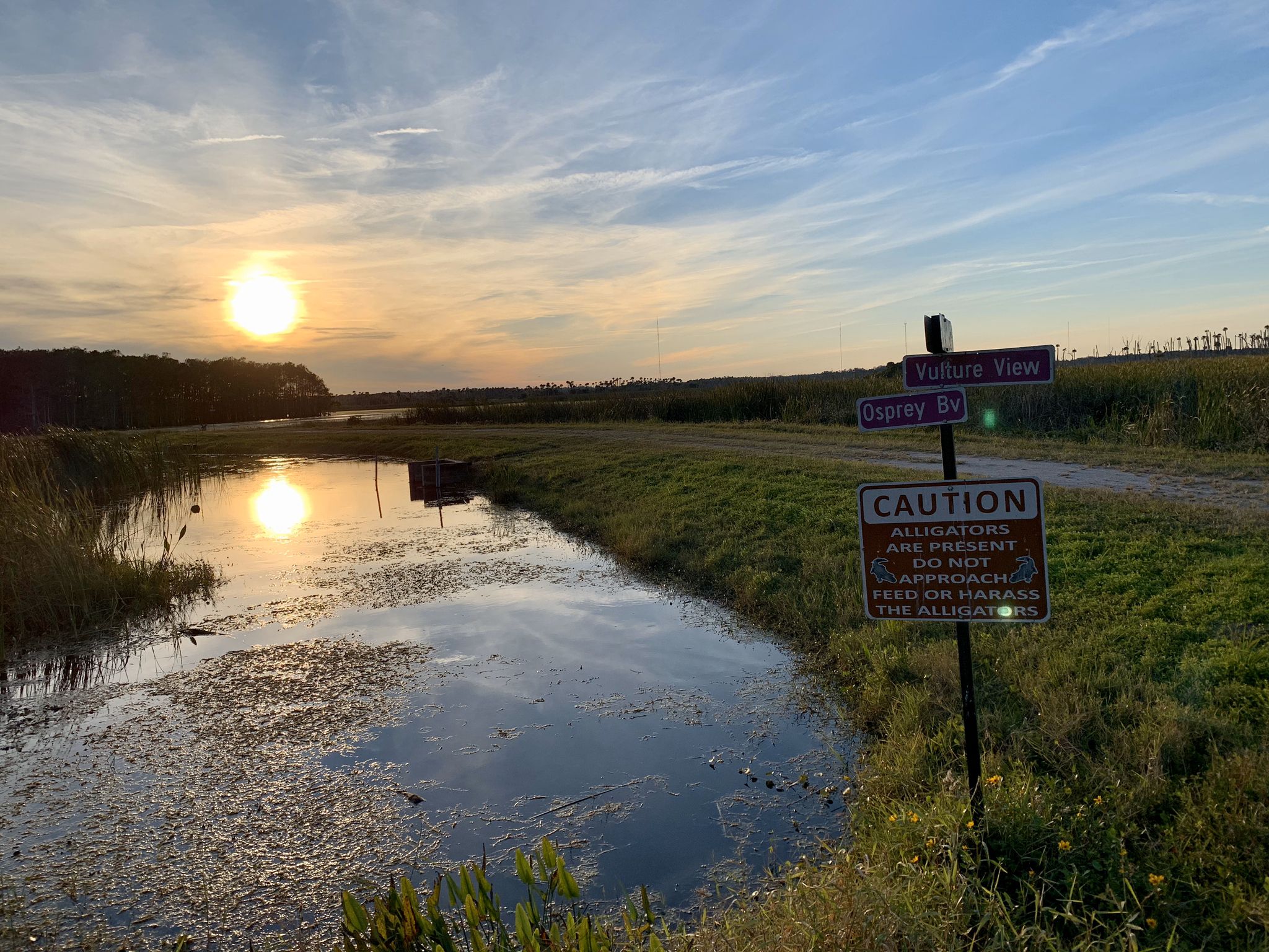 Sunset over a marshy waterway with a warning sign and golden reflections. - Lake Searcy loop from Orlando Wetlands Park