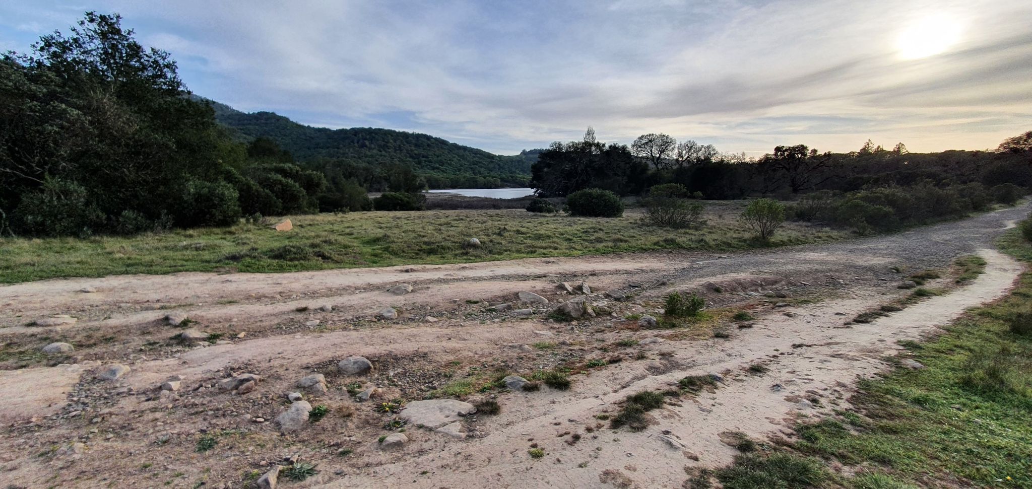 Dirt roads in a green field lead to a lake and forested hills. - Channel Trail – Lake Ilsanjo loop from Maria Carrillo High School