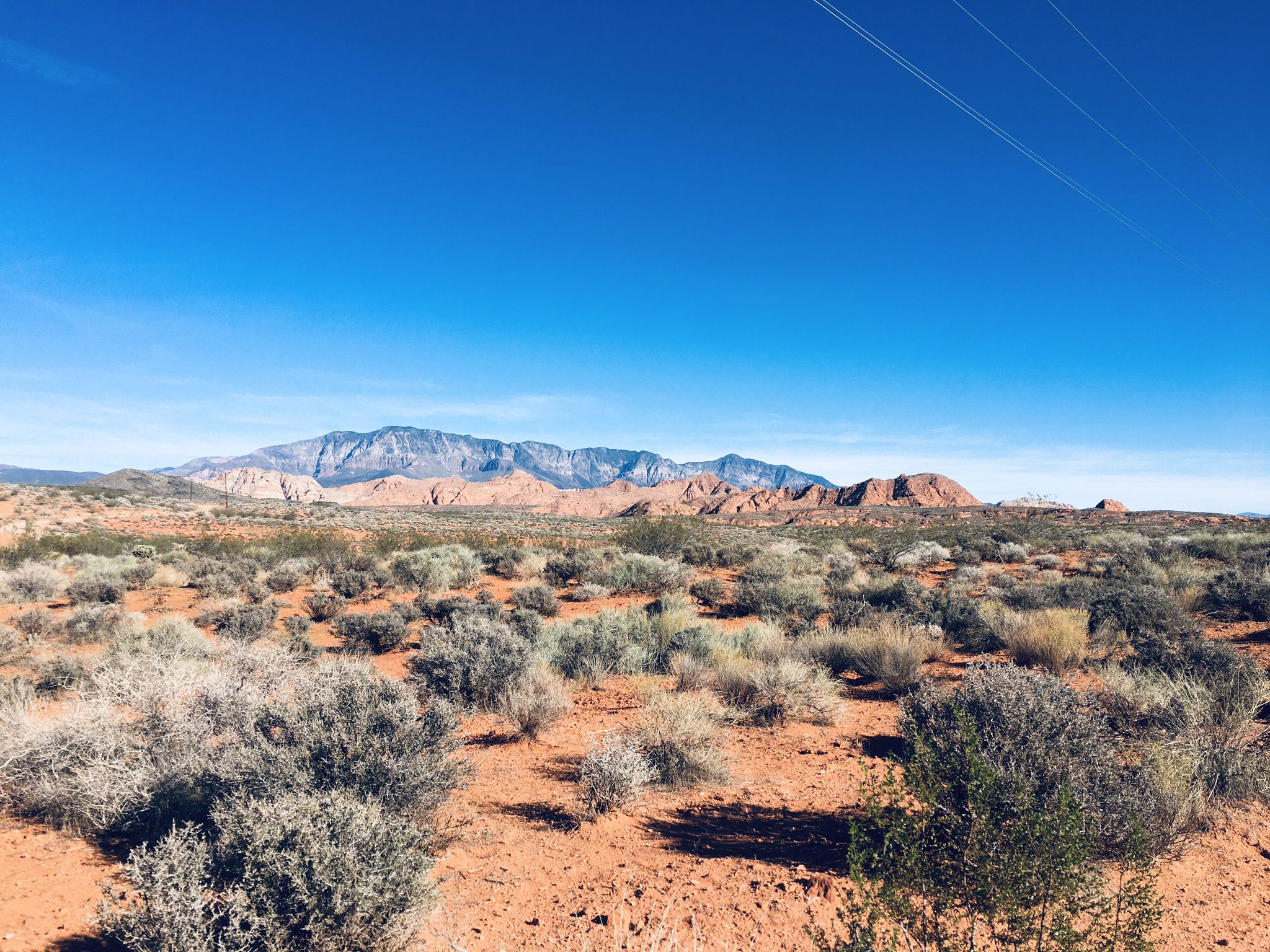 Wide desert landscape with brush, distant mountains, and power lines. - Dino Cliffs and Church Rocks Loop