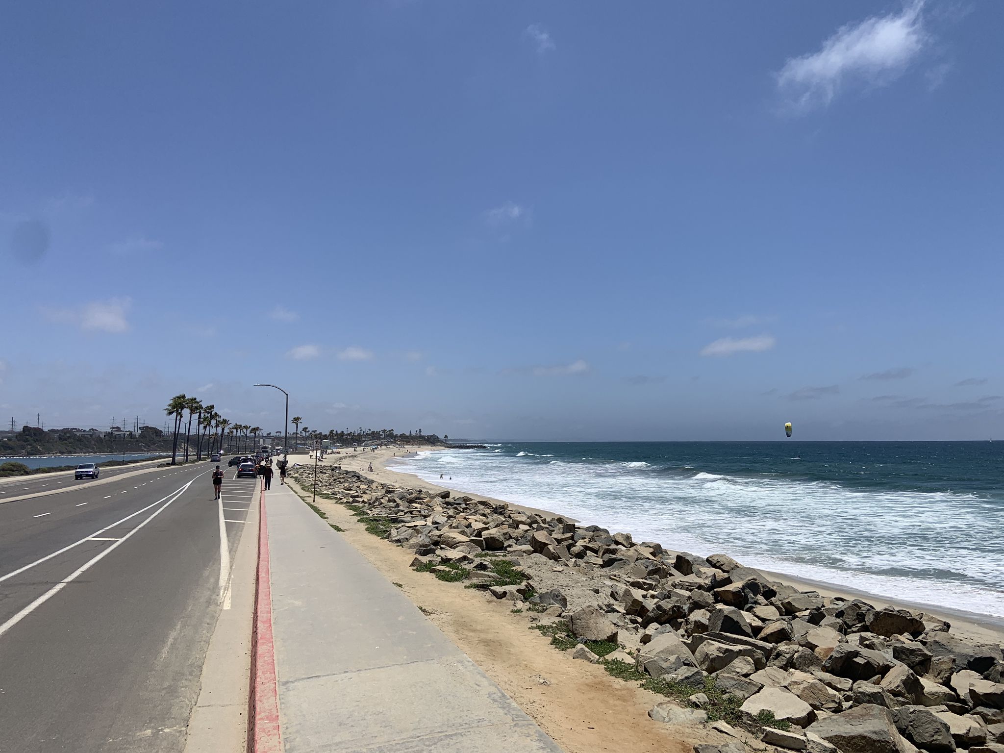 Sunny coastal road, rocky beach, ocean waves, and a distant kite surfer. - Tamarack Beach