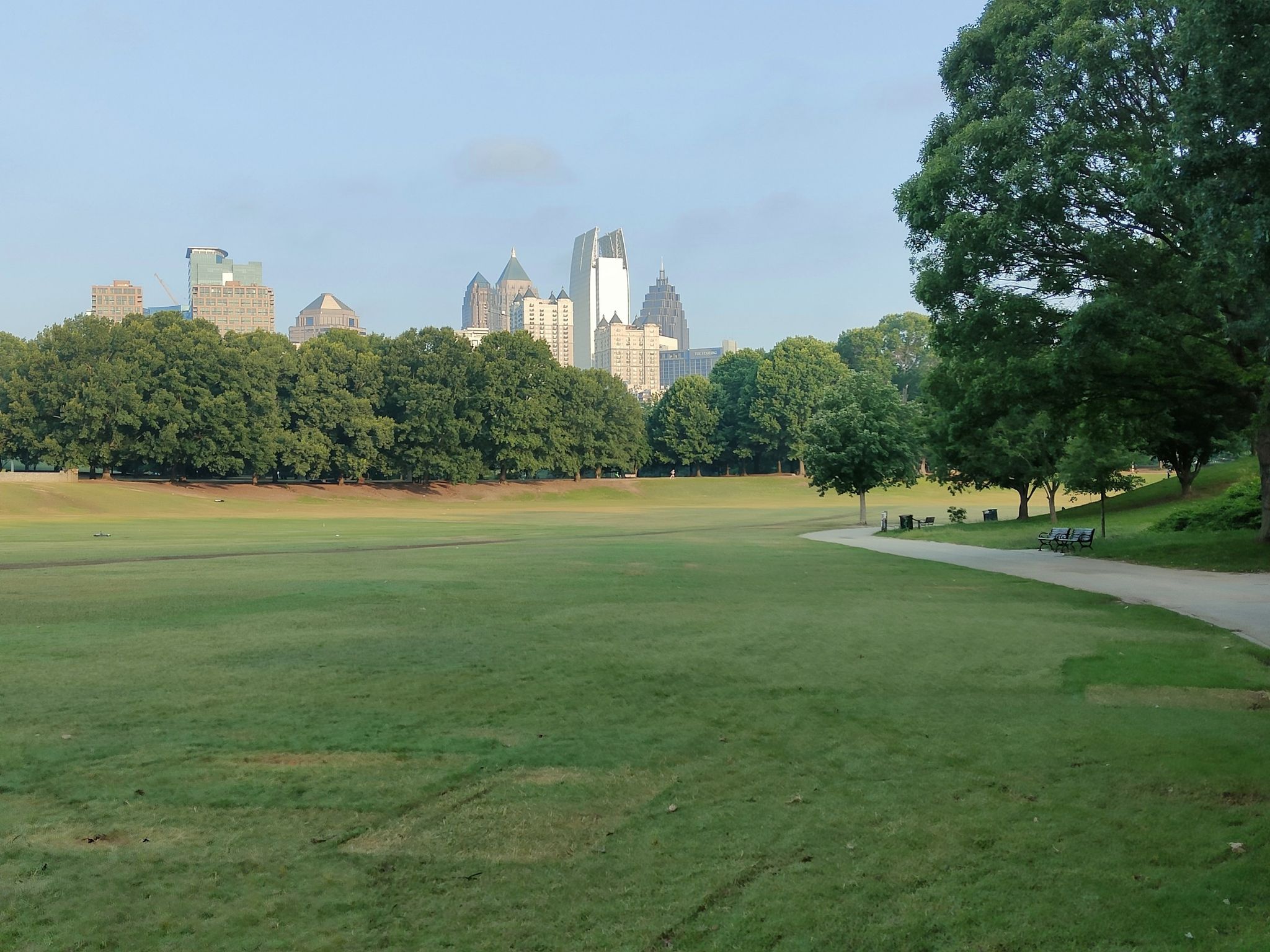 Expansive green field with trees, a paved path, and a distant city skyline. - Piedmont Park – Six Springs Wetlands loop from Noble Park