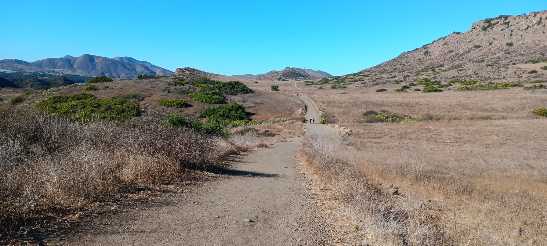 Dirt path winding through dry, sunny hills with distant mountains under blue sky. - Lizard Rock and Paradise Falls Loop