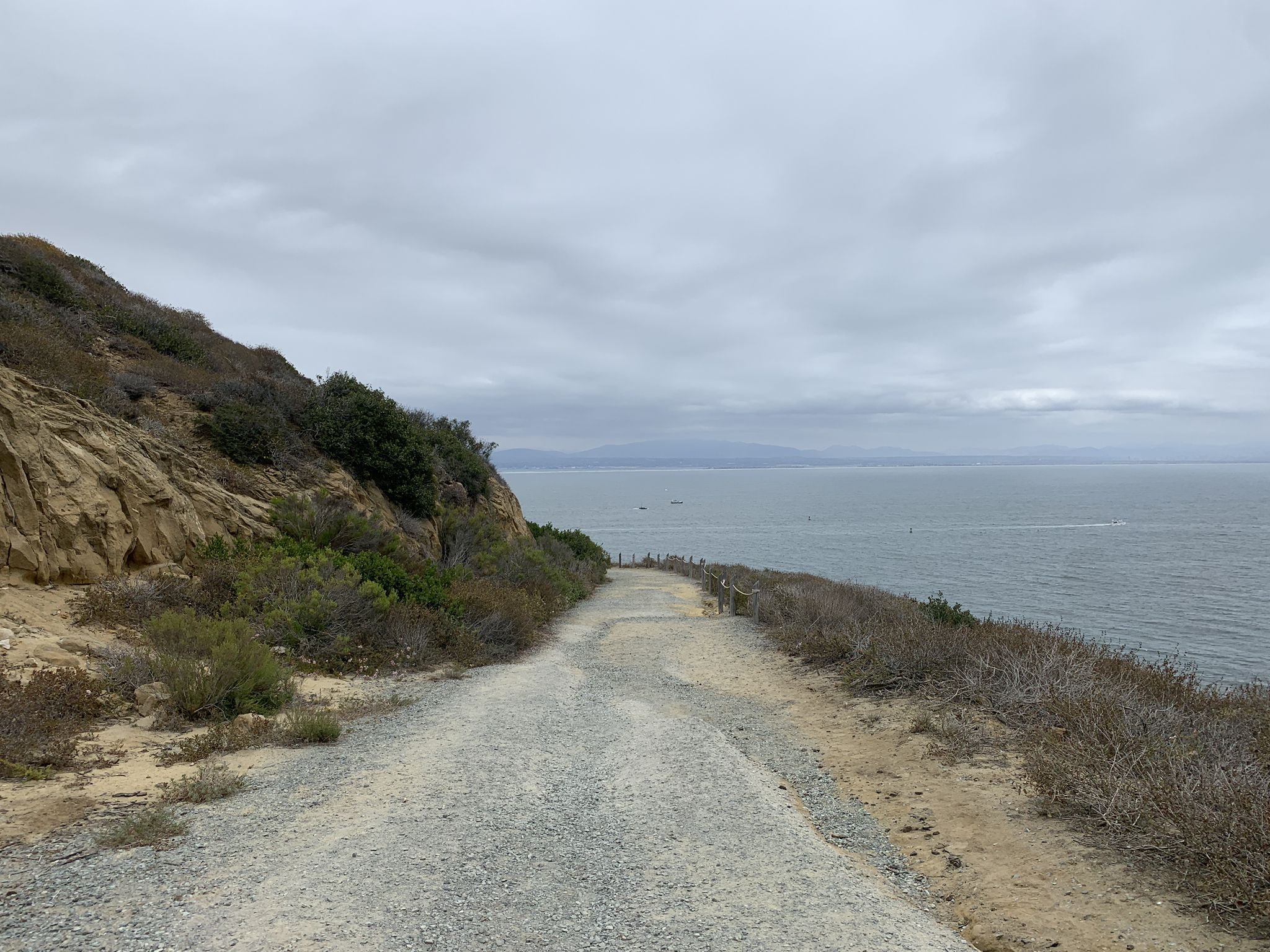 Gravel path along a cliff edge overlooking the ocean under an overcast sky. - Bayside Trail