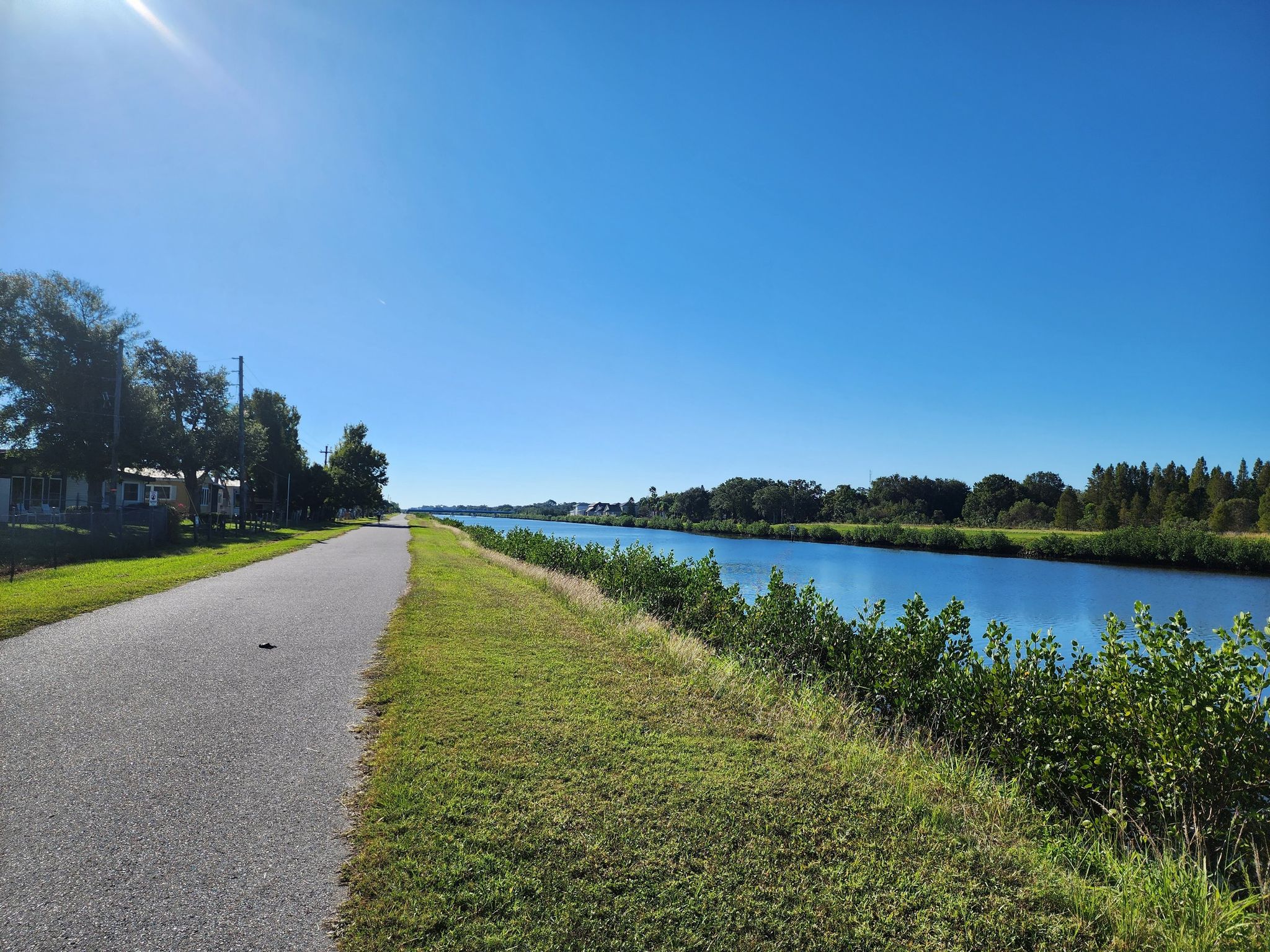 Sunny day with a paved path alongside a calm canal and green banks. - Honeymoon Island to Oldsmar Trail