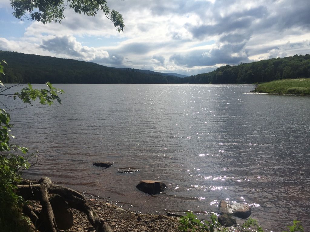 Sparkling lake water with forested hills and a cloudy, bright sky. - North Lake South Lake Trail