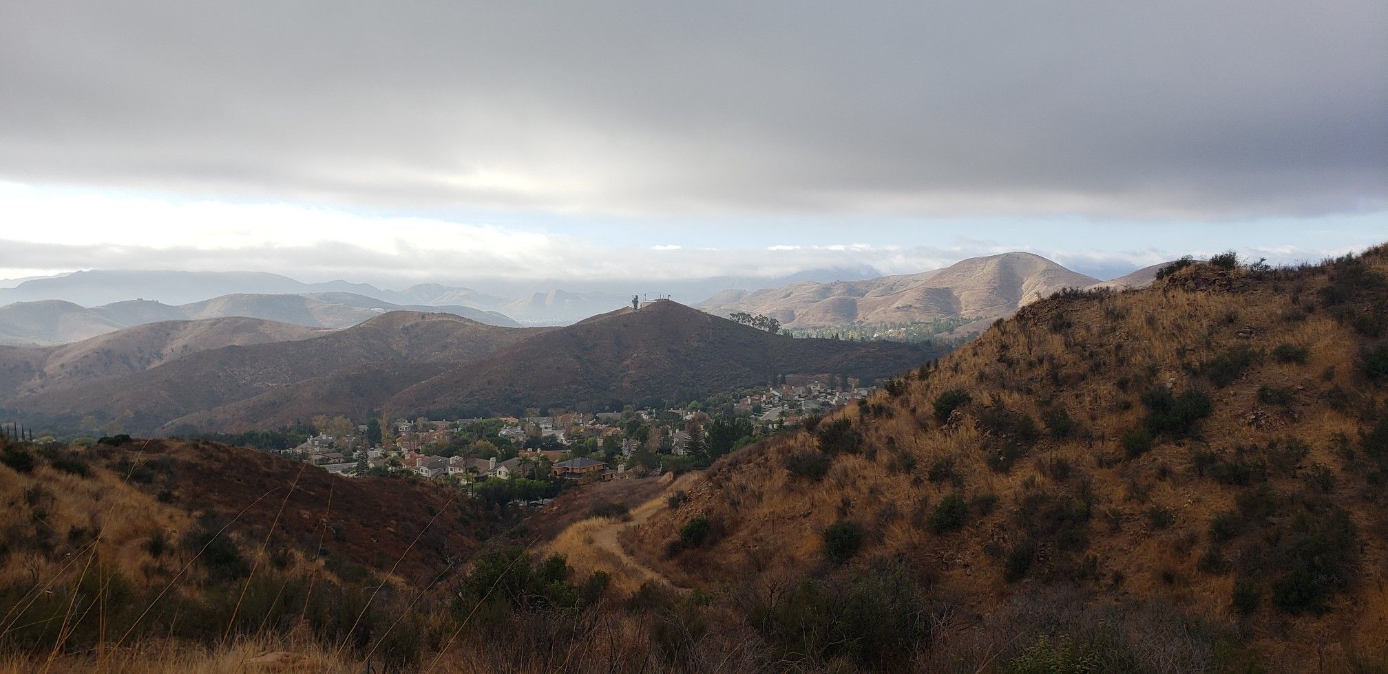 Panoramic view of dry, rolling hills and a distant town under a cloudy sky. - "Dead Cow" & "Suicide Loop"