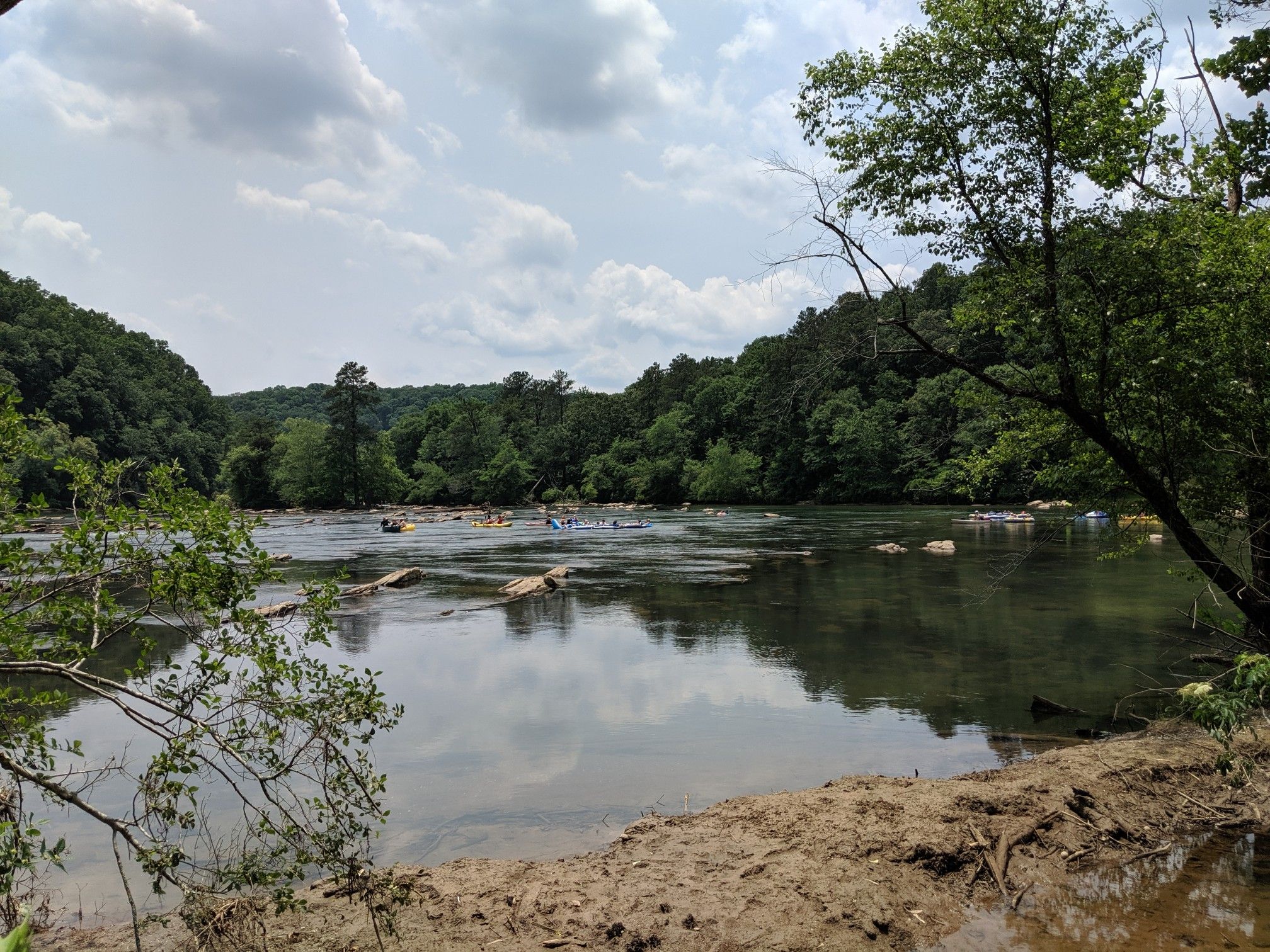 People floating on tubes in a river with forested banks, cloudy day. - East Palisades Trail