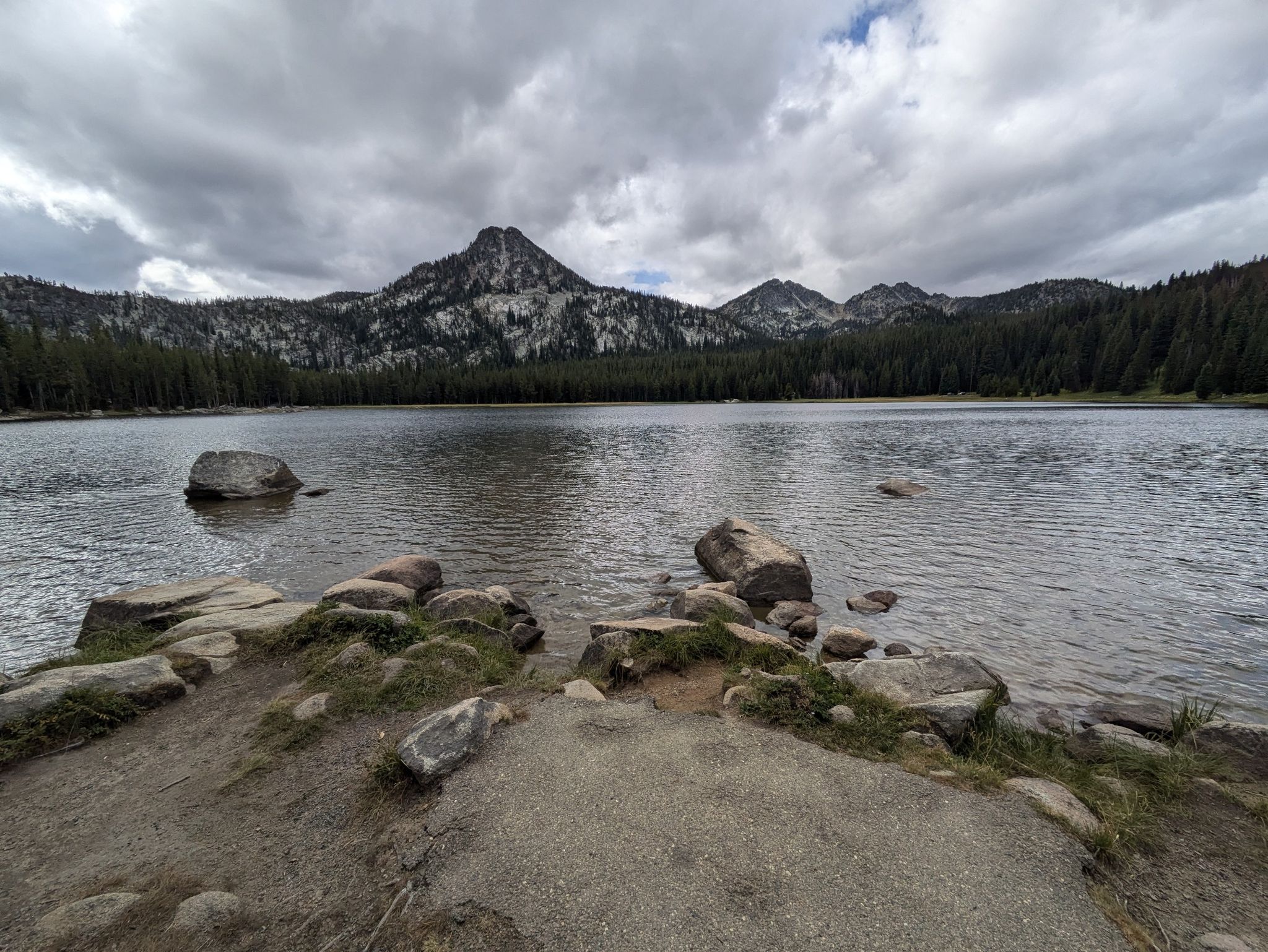 Calm lake with rocky shore, backed by pine forests and mountains. - Anthony Lake Shoreline Trail