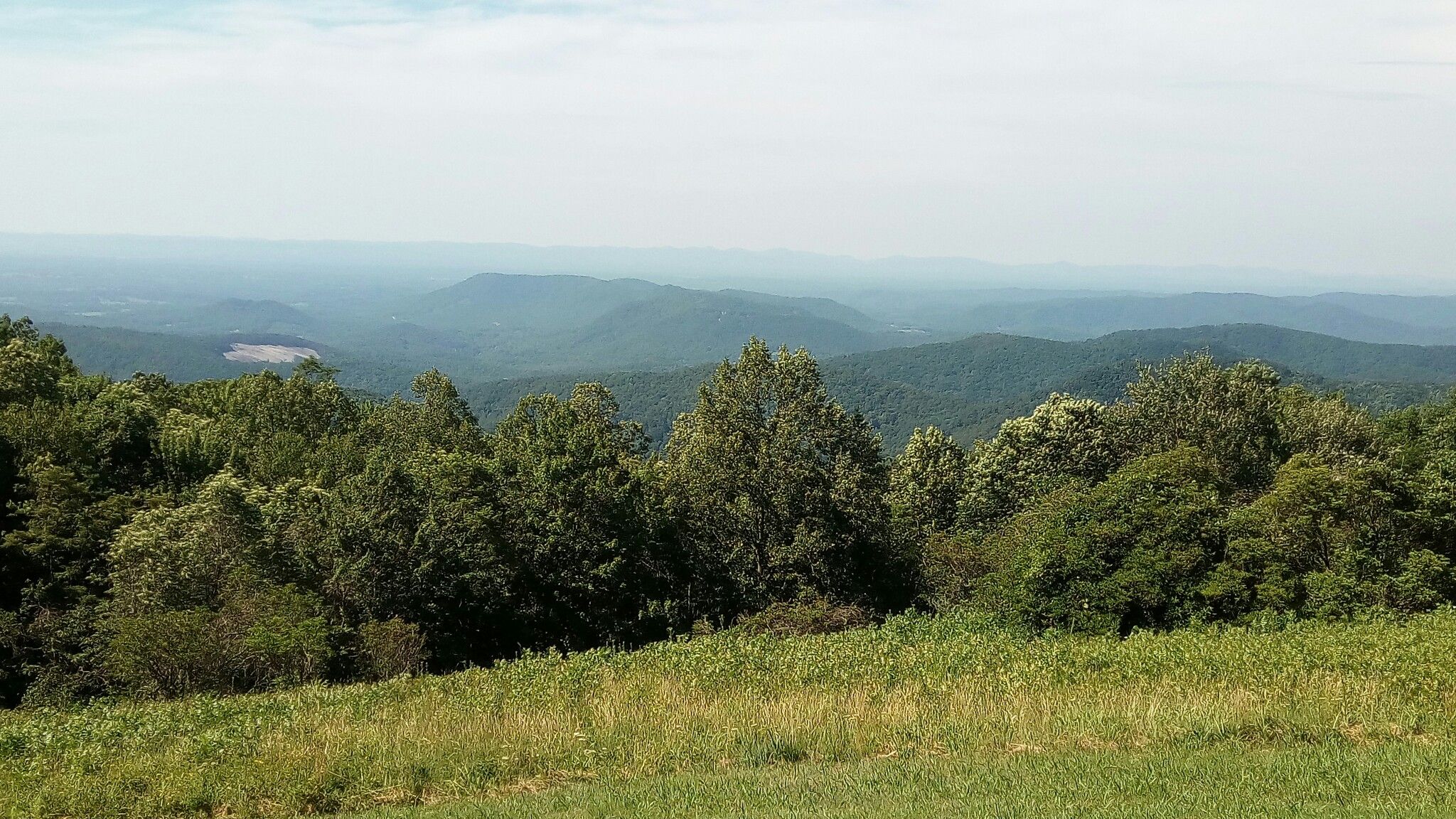 Expansive mountain vista with green forests and hazy distant peaks on a clear day. - North Line Trace