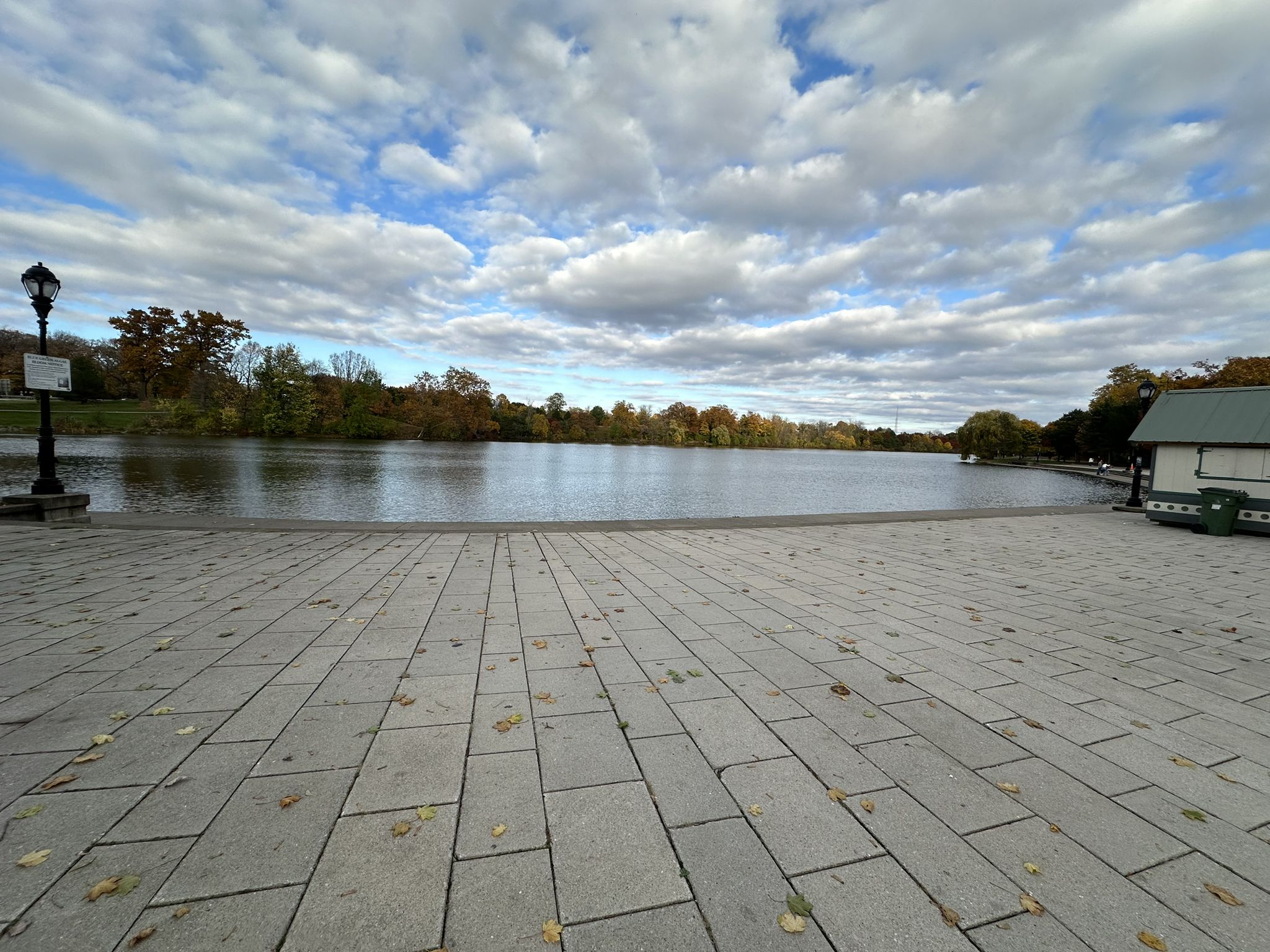 Paved plaza overlooking a calm lake with distant trees under cloudy sky. - Delaware Park – Hoyt Lake loop from LaSalle