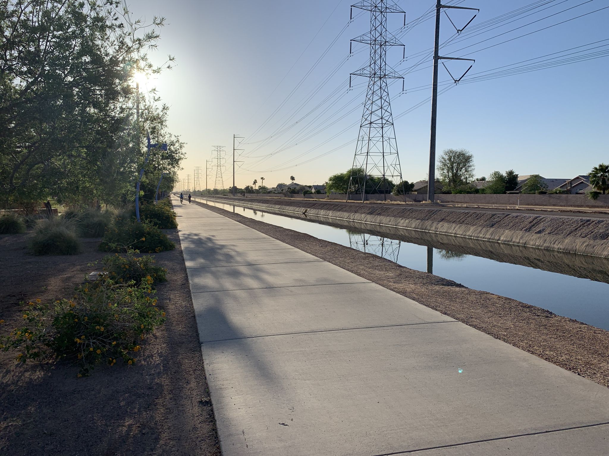 Two people walk on a sunny path next to a water canal and power lines. - Sun Circle Trail Canal Bike Path – Pavilion at McQueen Park loop from McClintock Dr & Southshore Dr