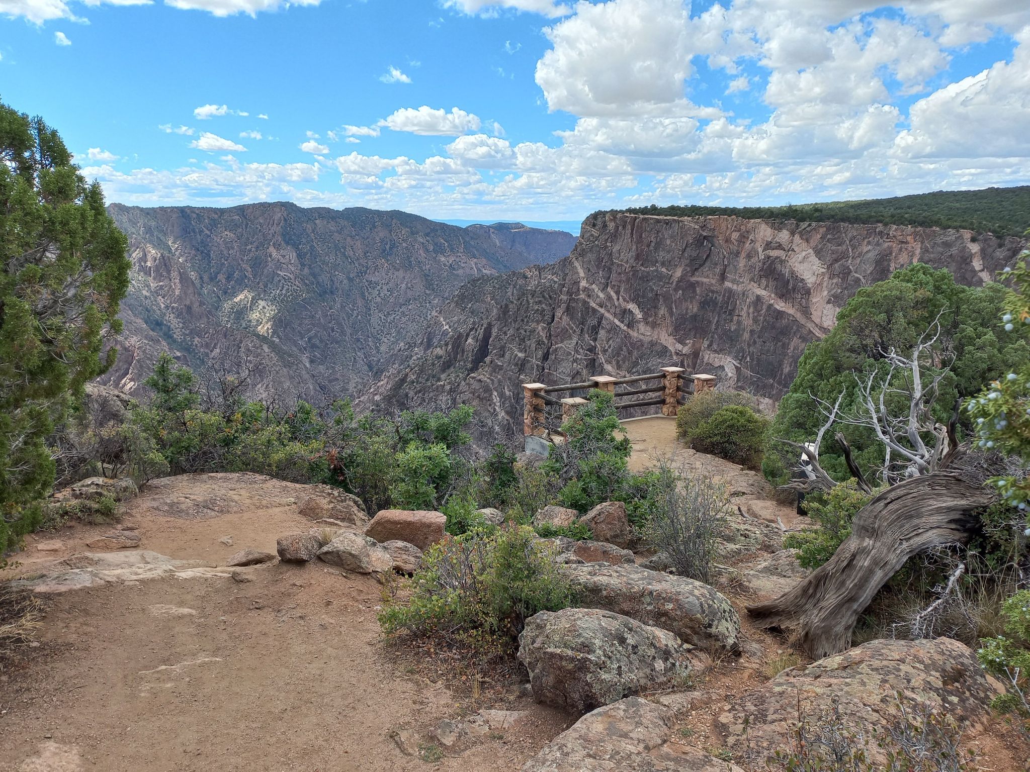 A scenic overlook with a wooden railing offers views of a deep canyon. - Black Canyon Scenic Drive