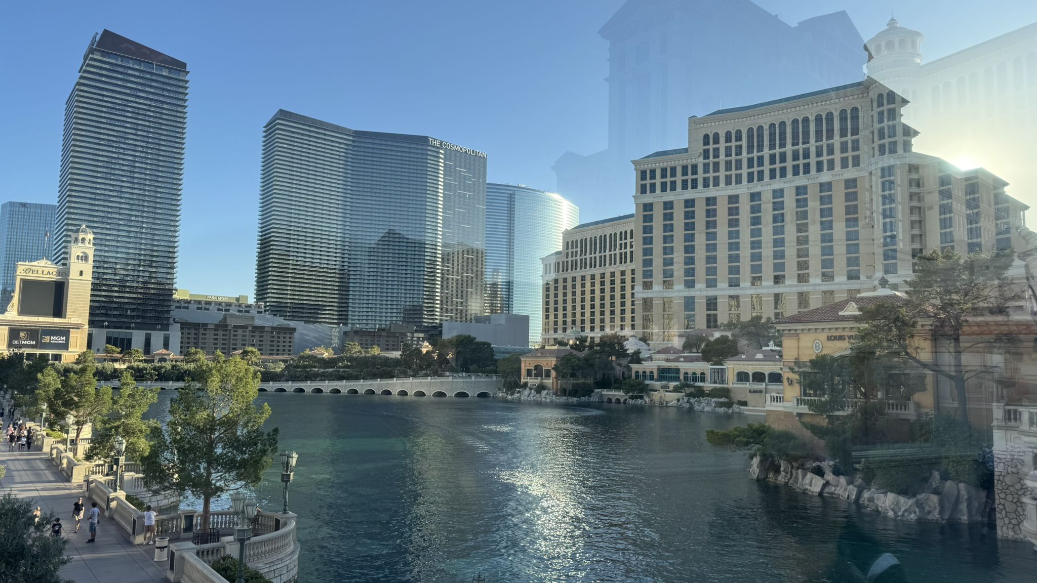Modern and classical buildings line a large body of water under a bright sky. - The Cosmopolitan – The MGM Grand loop from Westgate