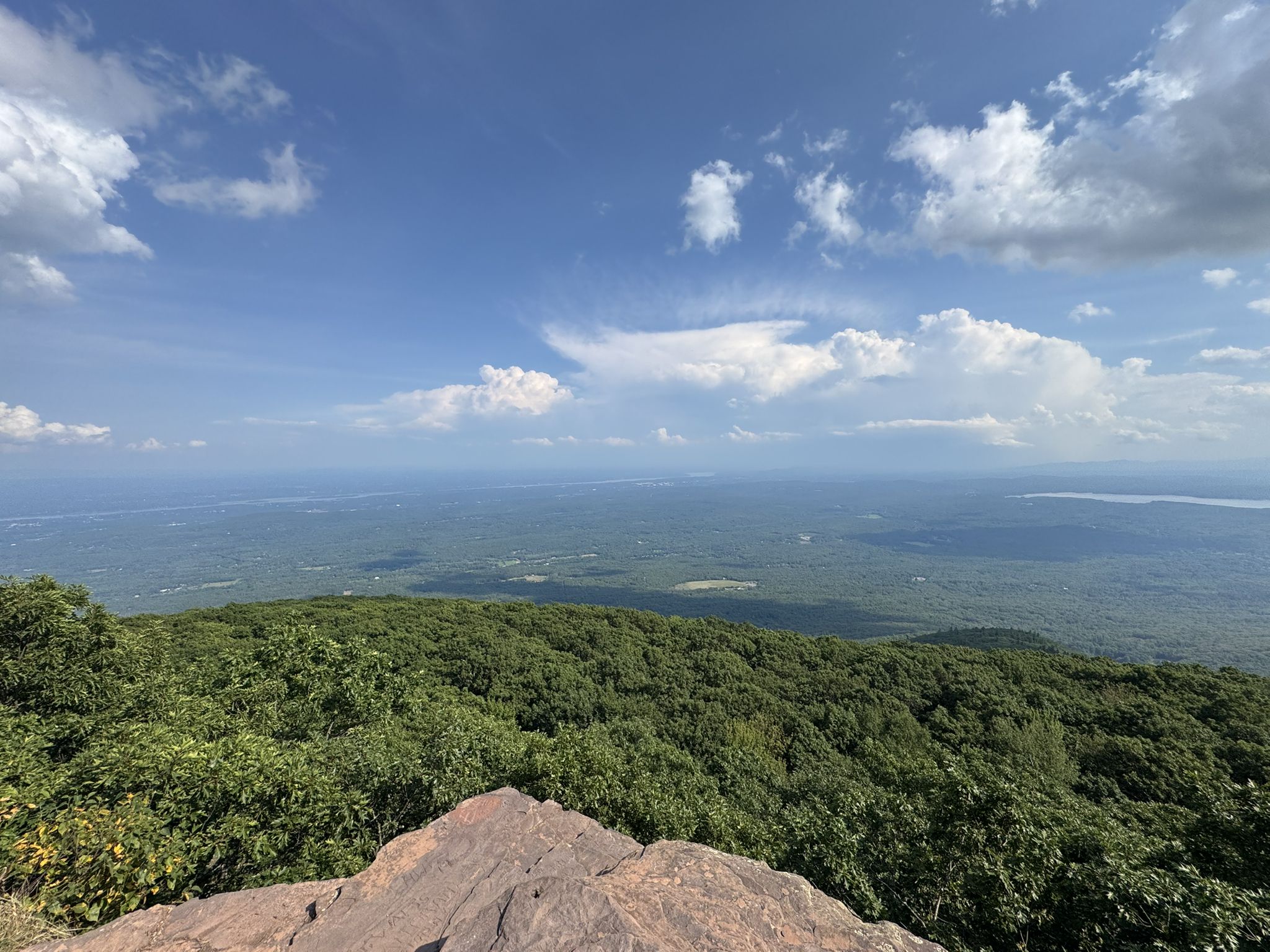 Rocky foreground overlooking a vast green forest and distant horizon under blue sky. - Overlook Spur Trail