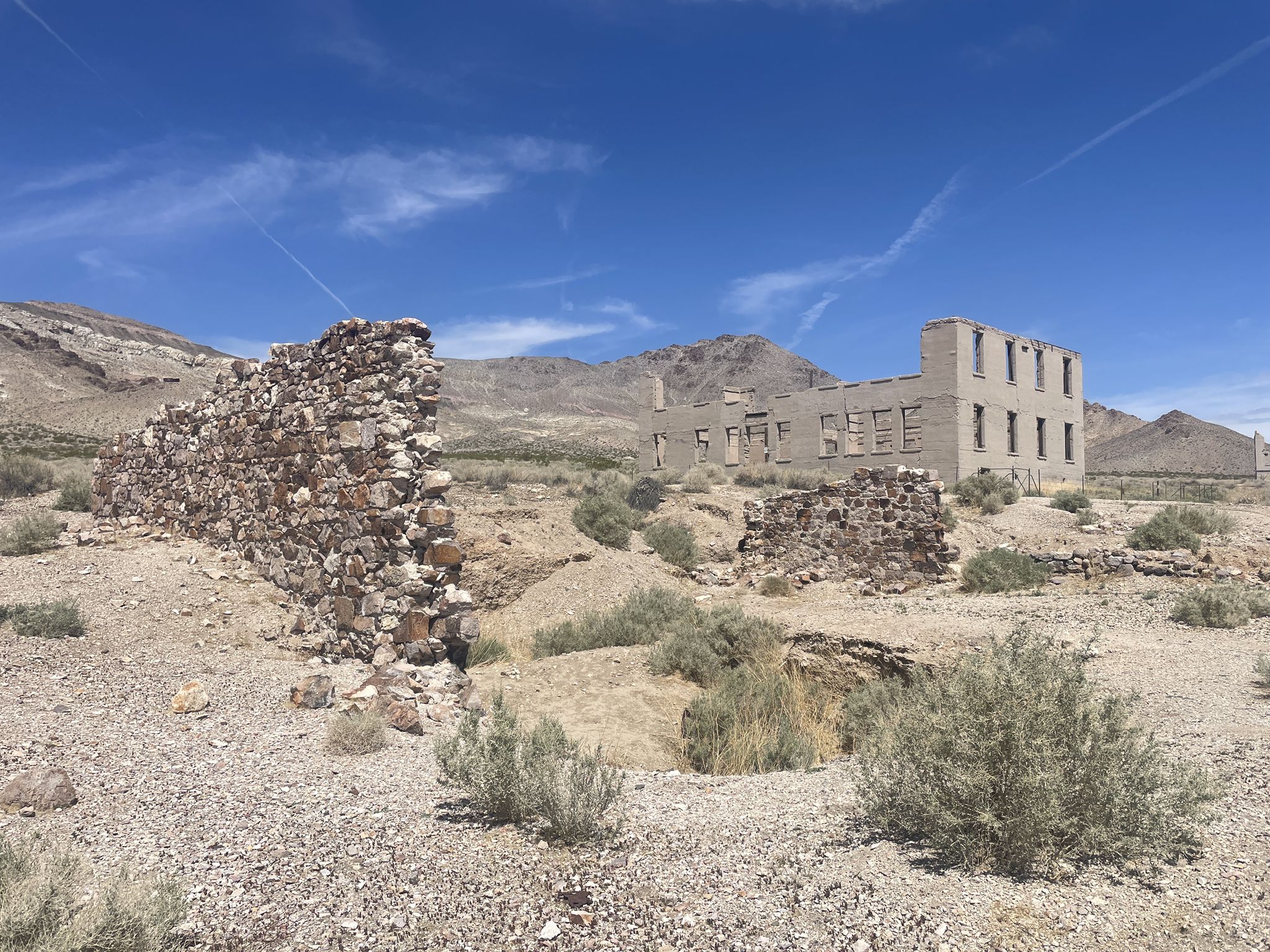 Desert ruins with stone walls and a partially standing building under a clear sky. - Rhyolite Ghost Town Trail