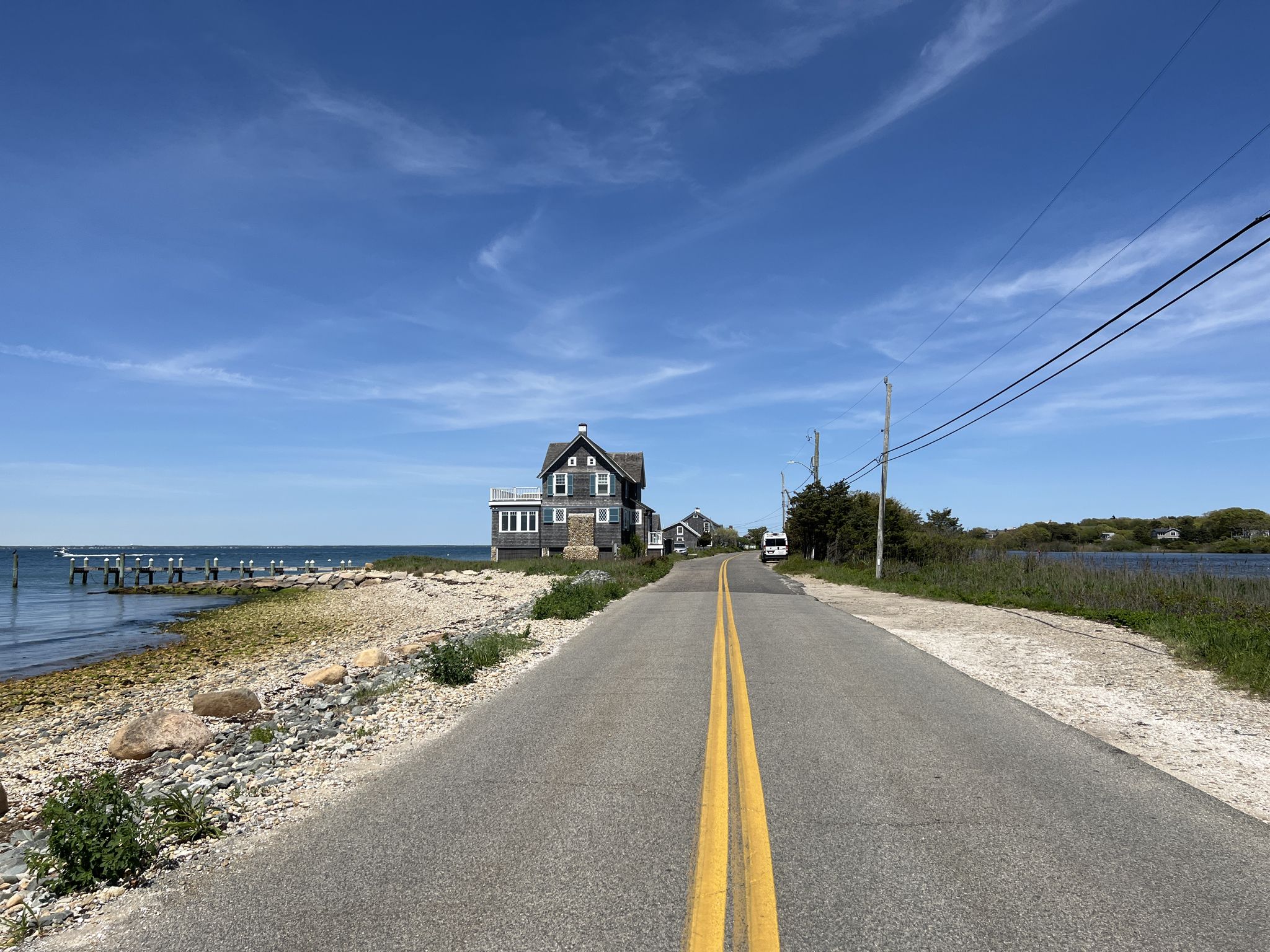 Road leading to a house by the water, with a distant pier. - East Chop Lighthouse – Nobska Lighthouse loop from Oak Bluffs