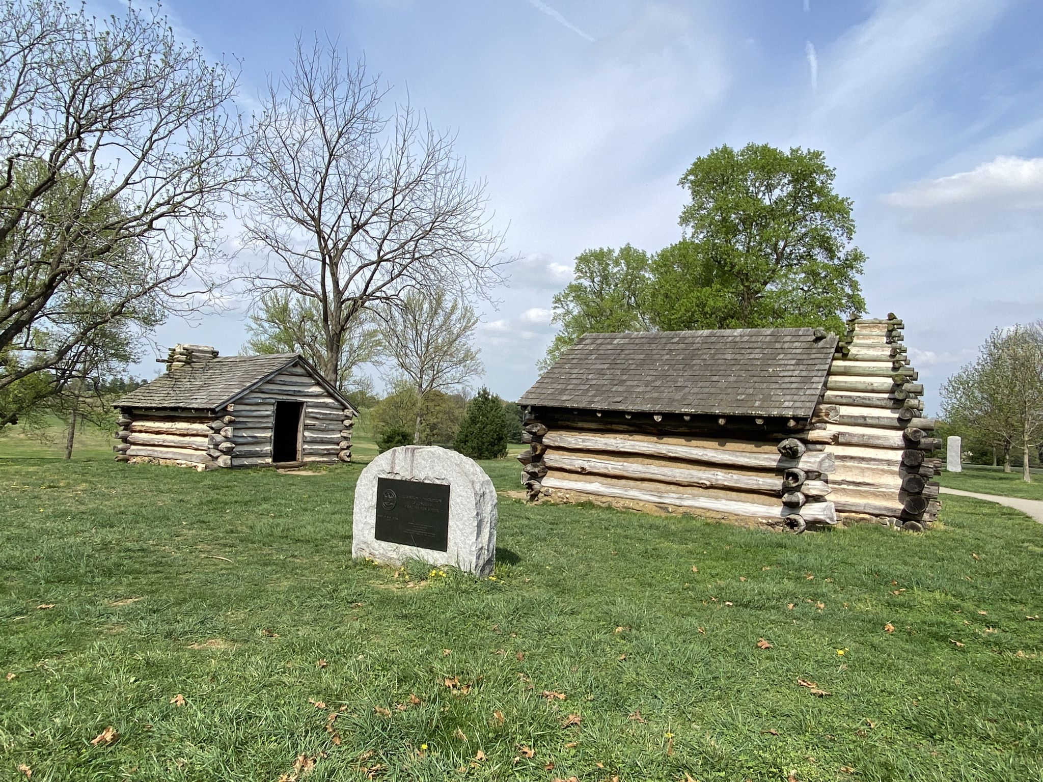 Two log cabins and a stone marker on green grass, partly cloudy sky. - National Memorial Arch – Knox Covered Bridge loop from Wayne